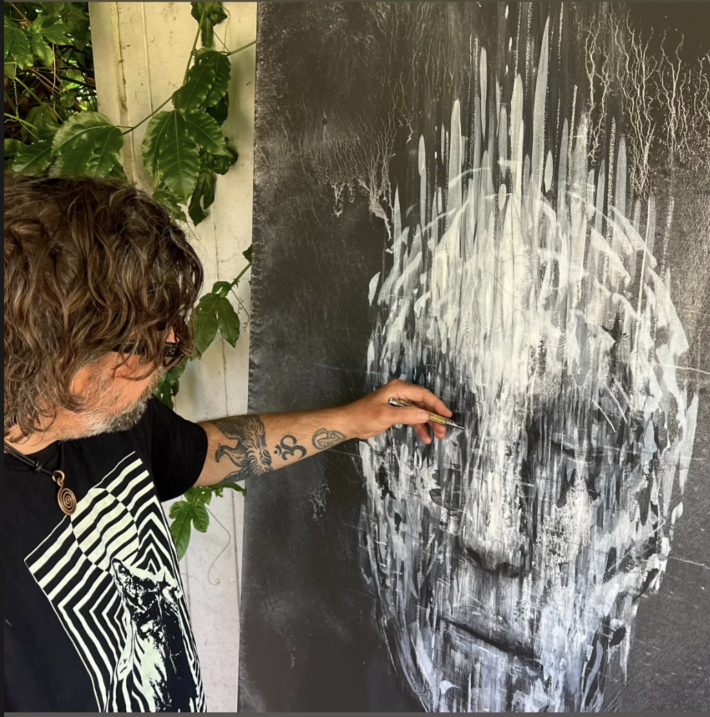 An artist creating a black and white portrait of a man's face on a large canvas with paint, using a brush.
