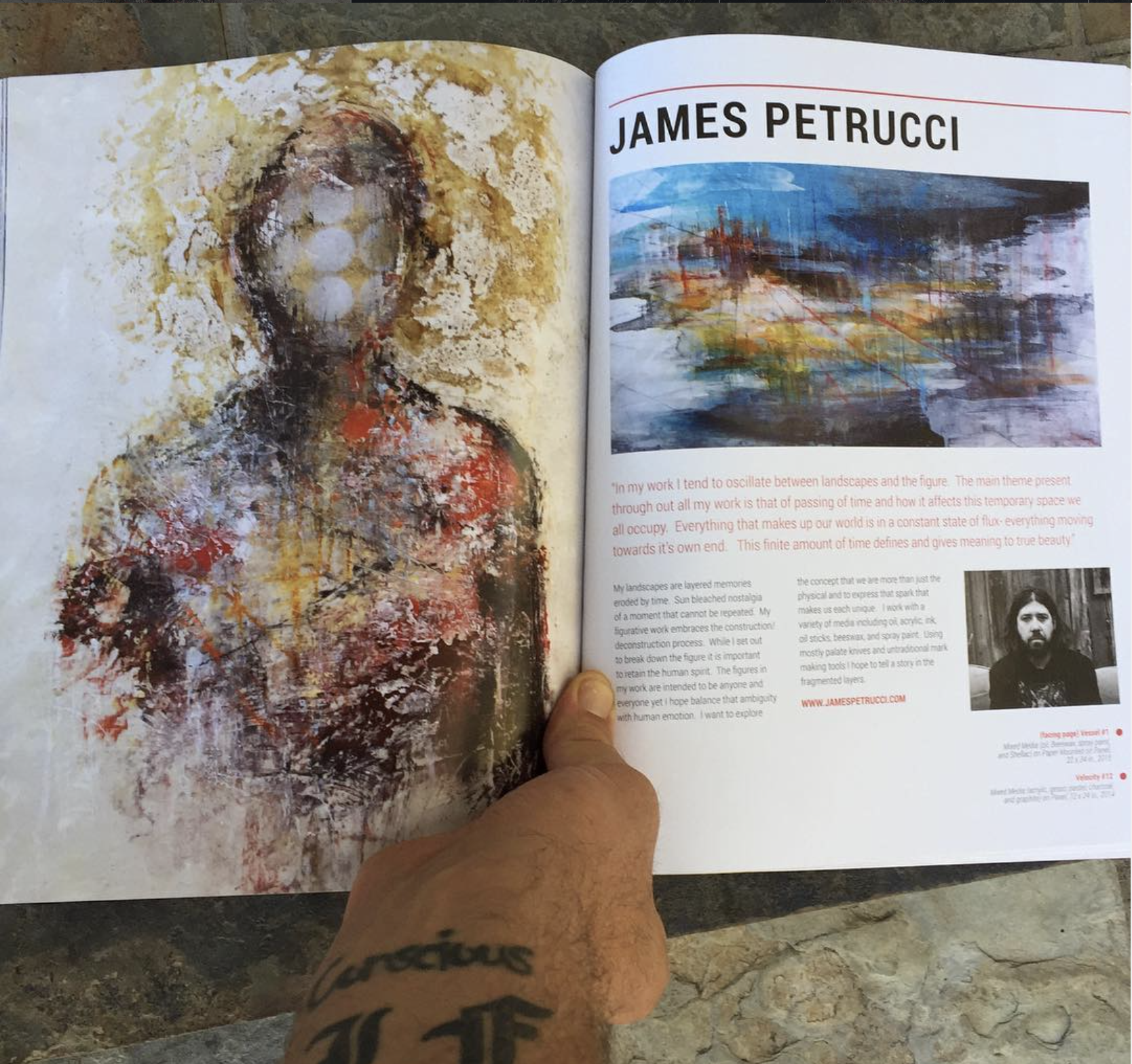 Open art magazine with abstract paintings and artist information, including a portrait of James Petrucci, on a stone surface.