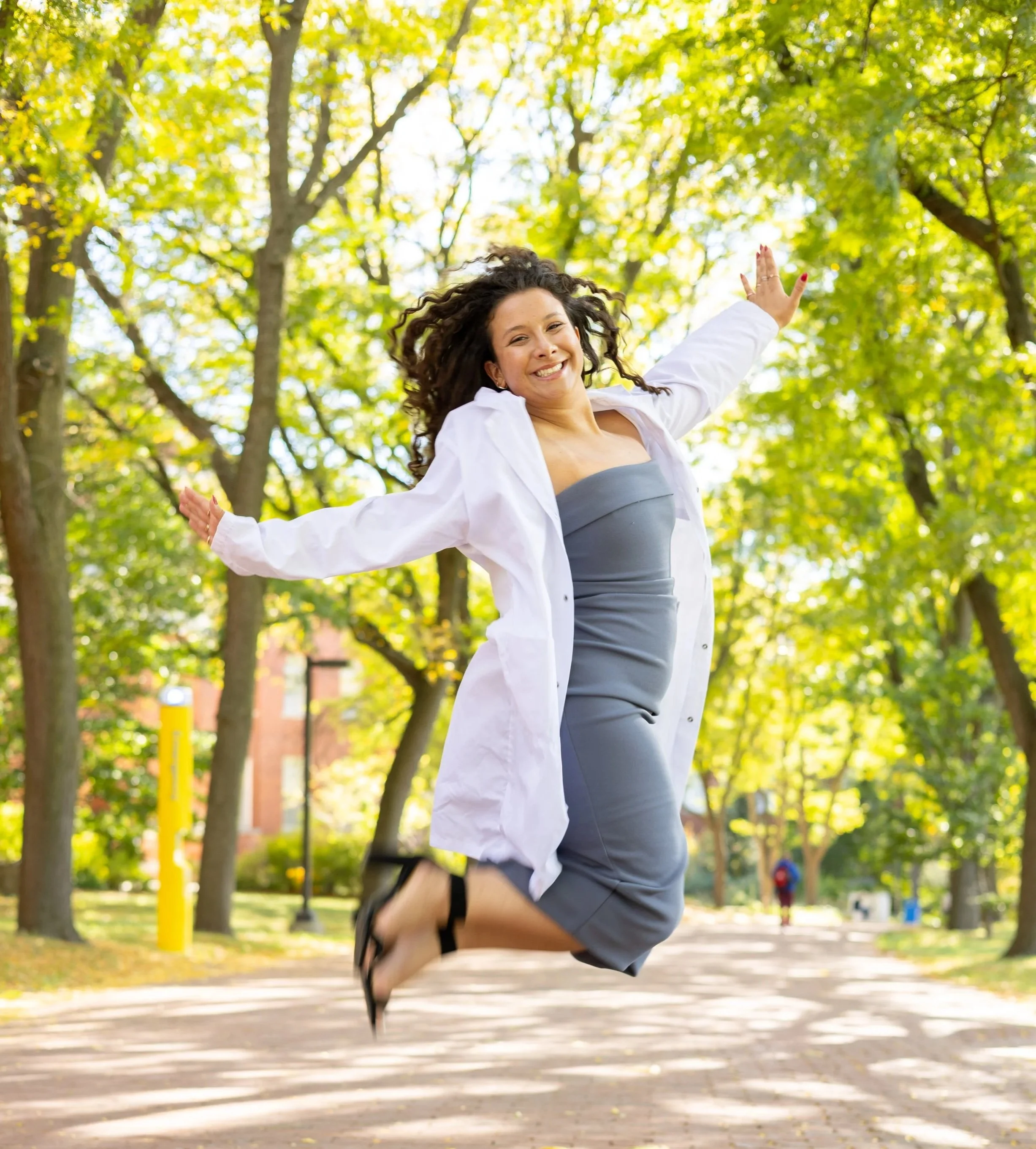 Young woman jumping in a park surrounded by green trees on a sunny day.