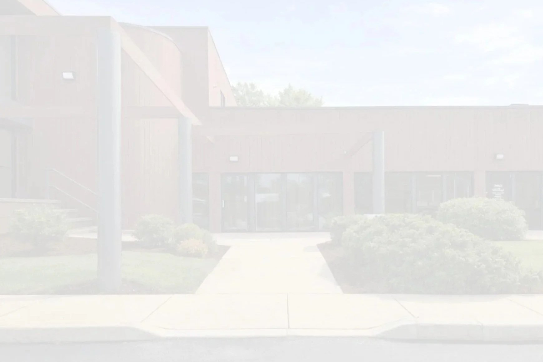 A building with a modern architectural style, featuring large glass doors, surrounded by landscaped bushes, under a partly cloudy sky.