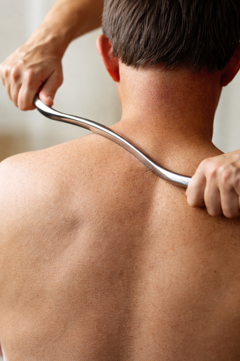 A person receiving a back massage with a metal tool on their upper back and neck, a treatment process used in Gonstead chiropractic.