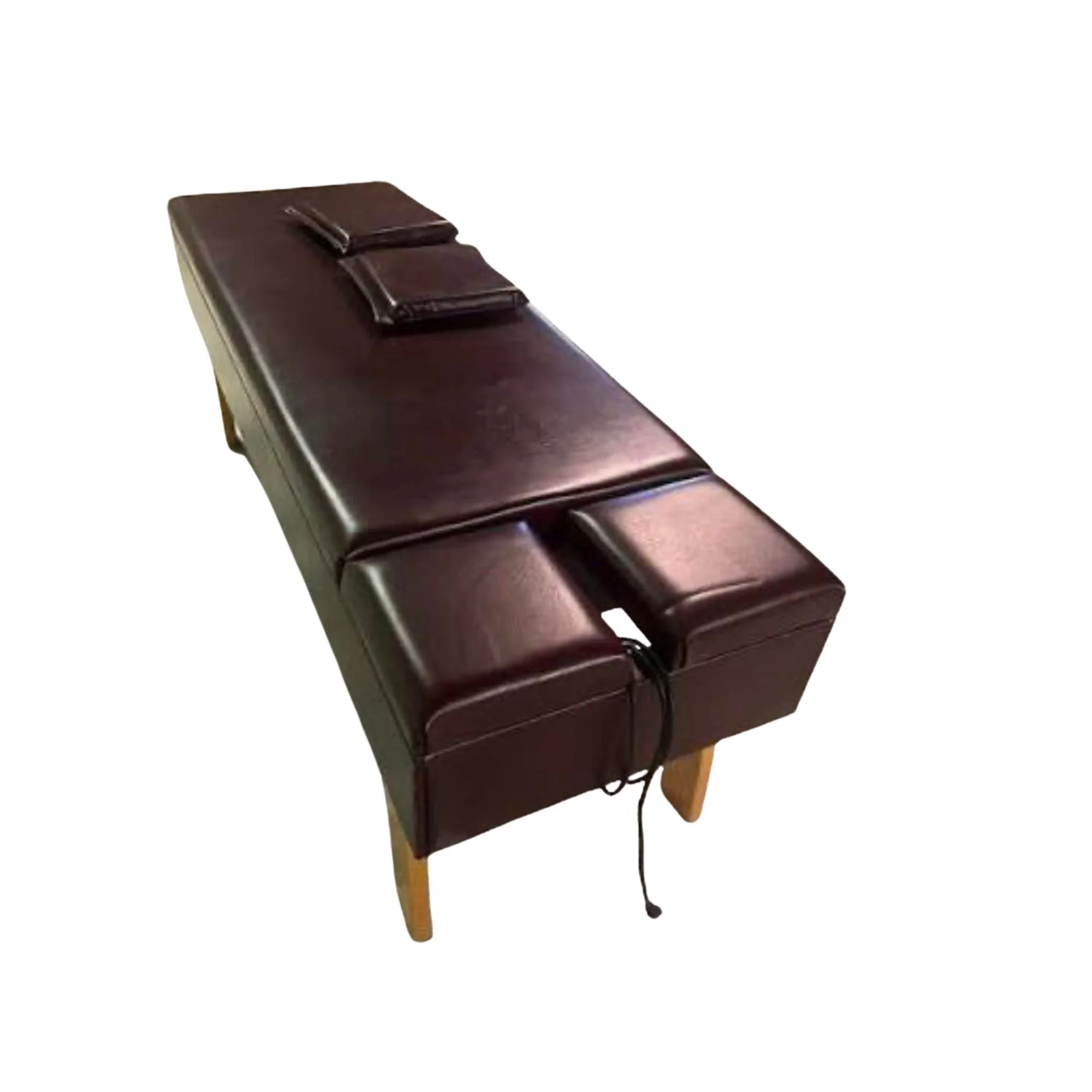 A long, rectangular, dark brown leather chiropractic table with two small pillows on top and a black cord hanging from the front.