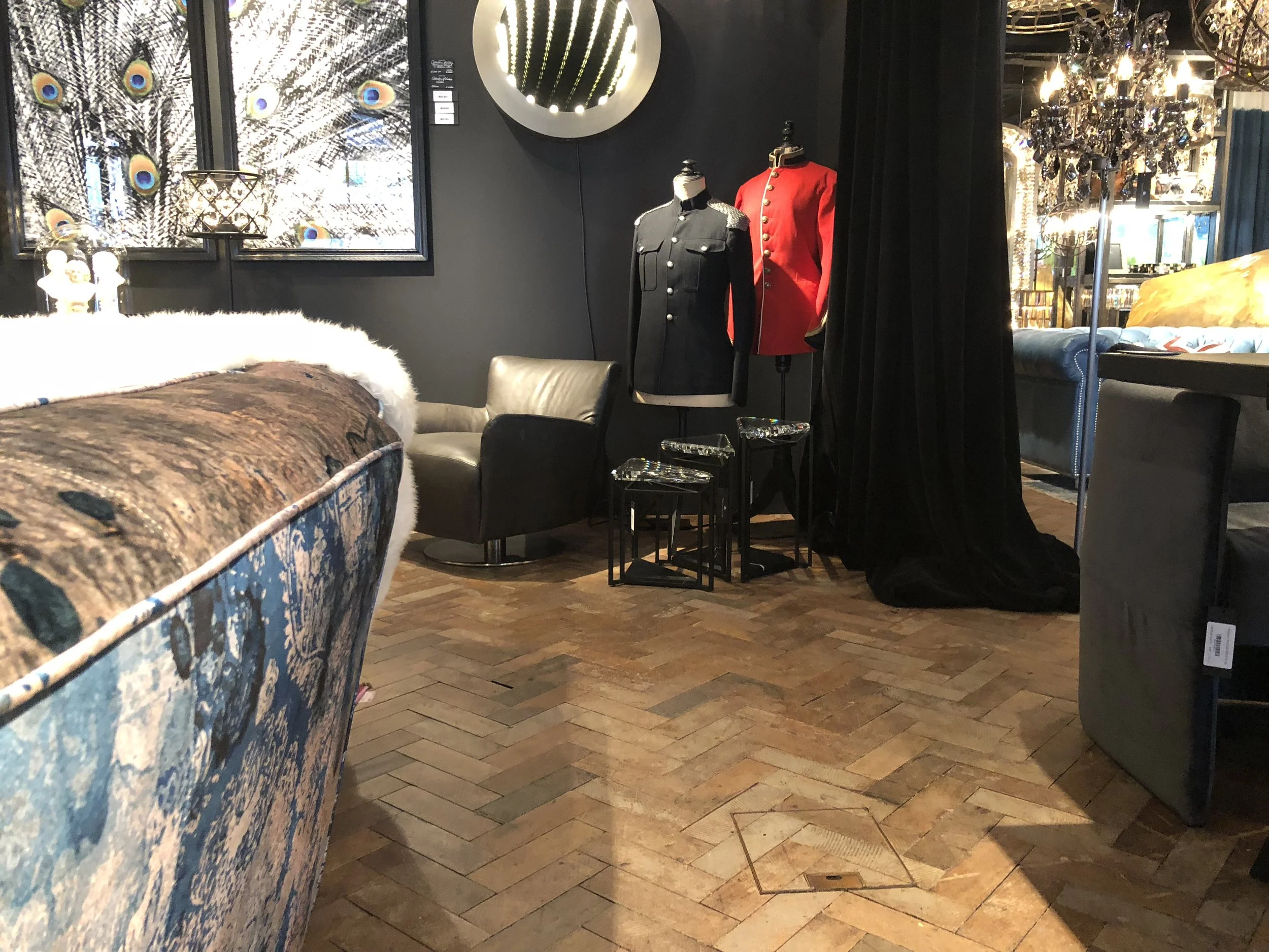 Interiores decorativos con sillas, maniquíes con uniformes, cortinas negras y lámparas de araña en un ambiente estilo vintage.