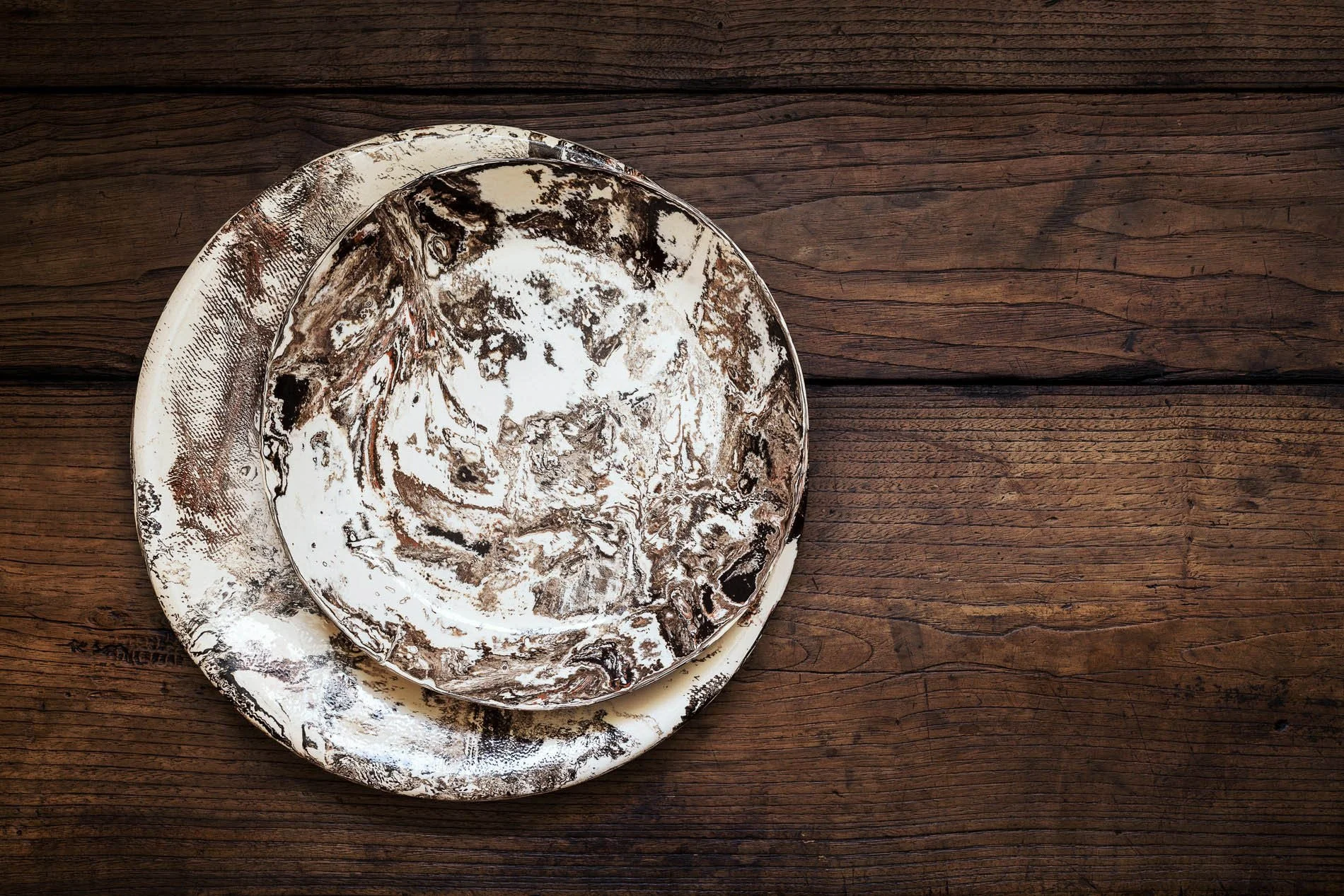 Platos de cerámica con patrones abstractos en tonos marrón, blanco y negro, colocados sobre una mesa de madera.