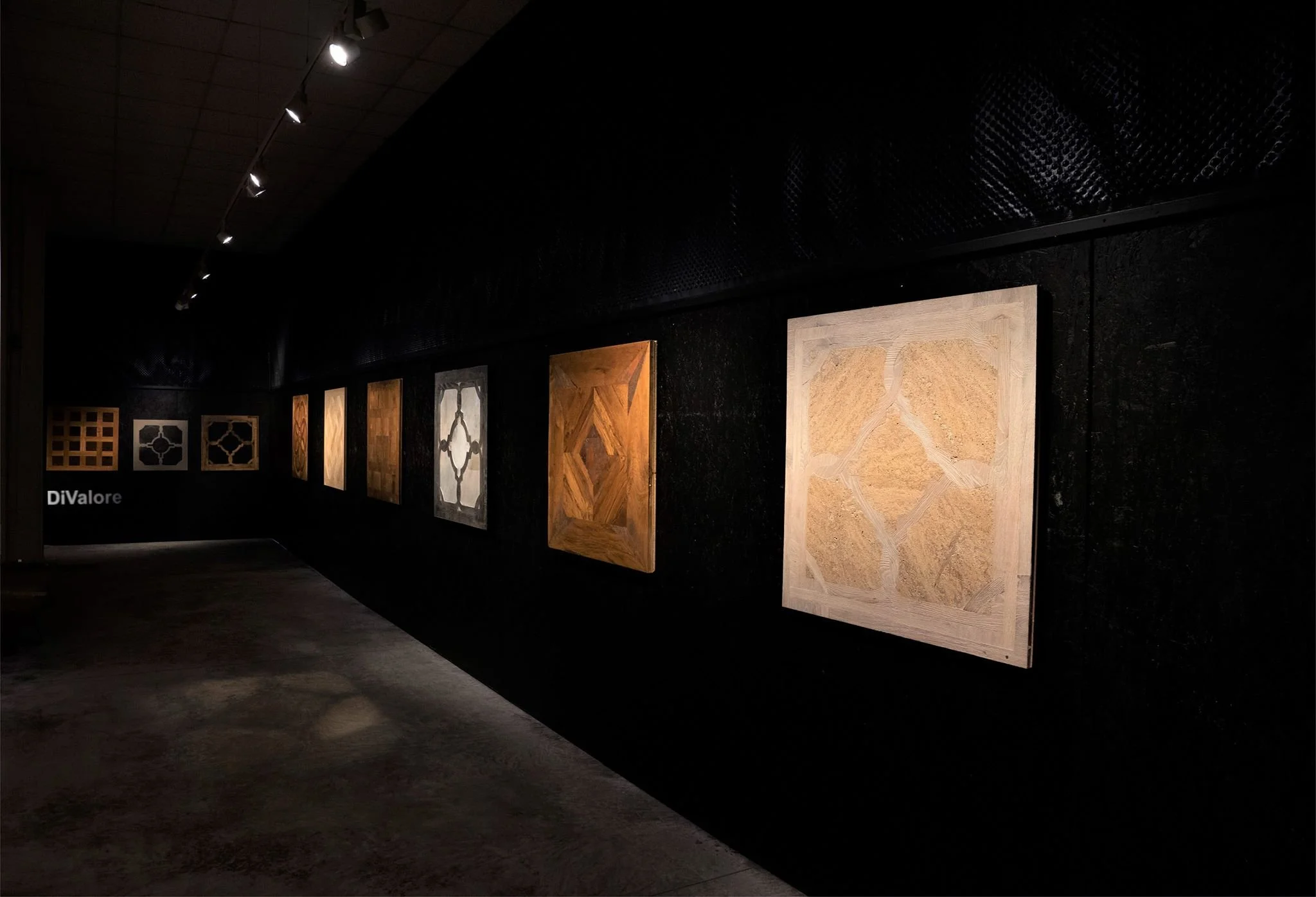 Galería de cuadros de madera en exhibición en una galería de arte con paredes negras y iluminación dirigida.