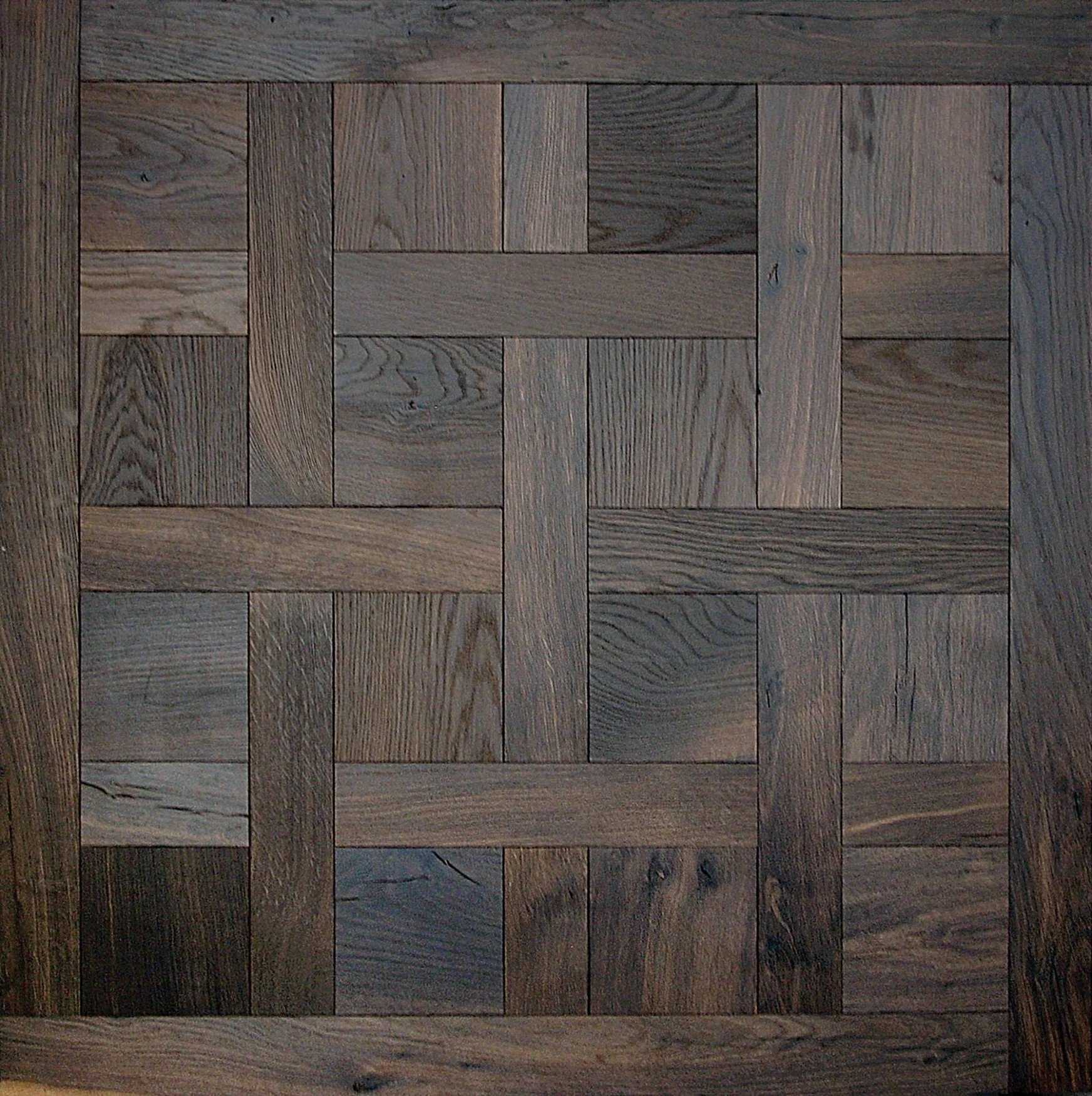 Piso de madera con patrón de tablas entrelazadas en tonos marrones y grises.