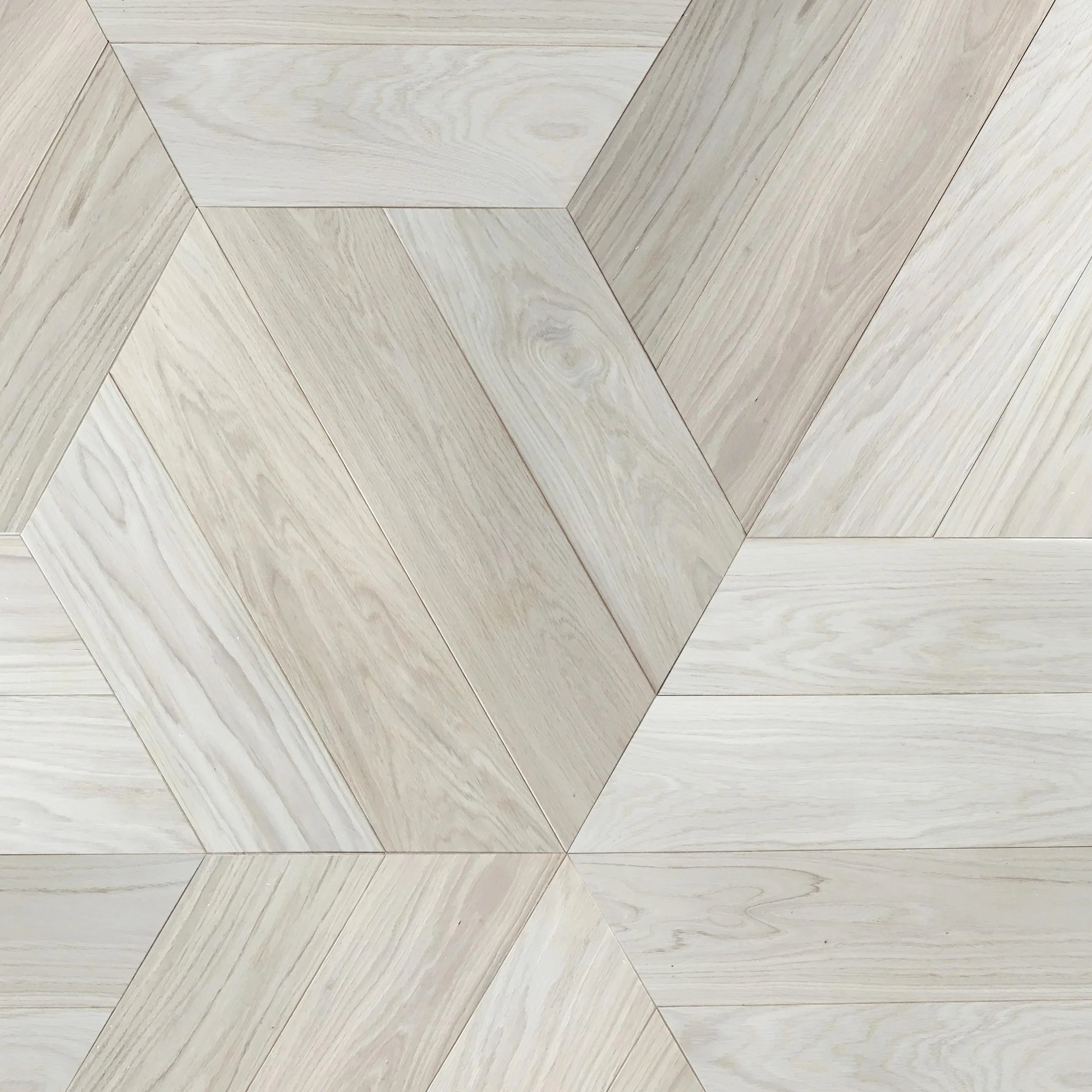 Detalles de un piso de madera en tonos claros, en patrón de diamante.