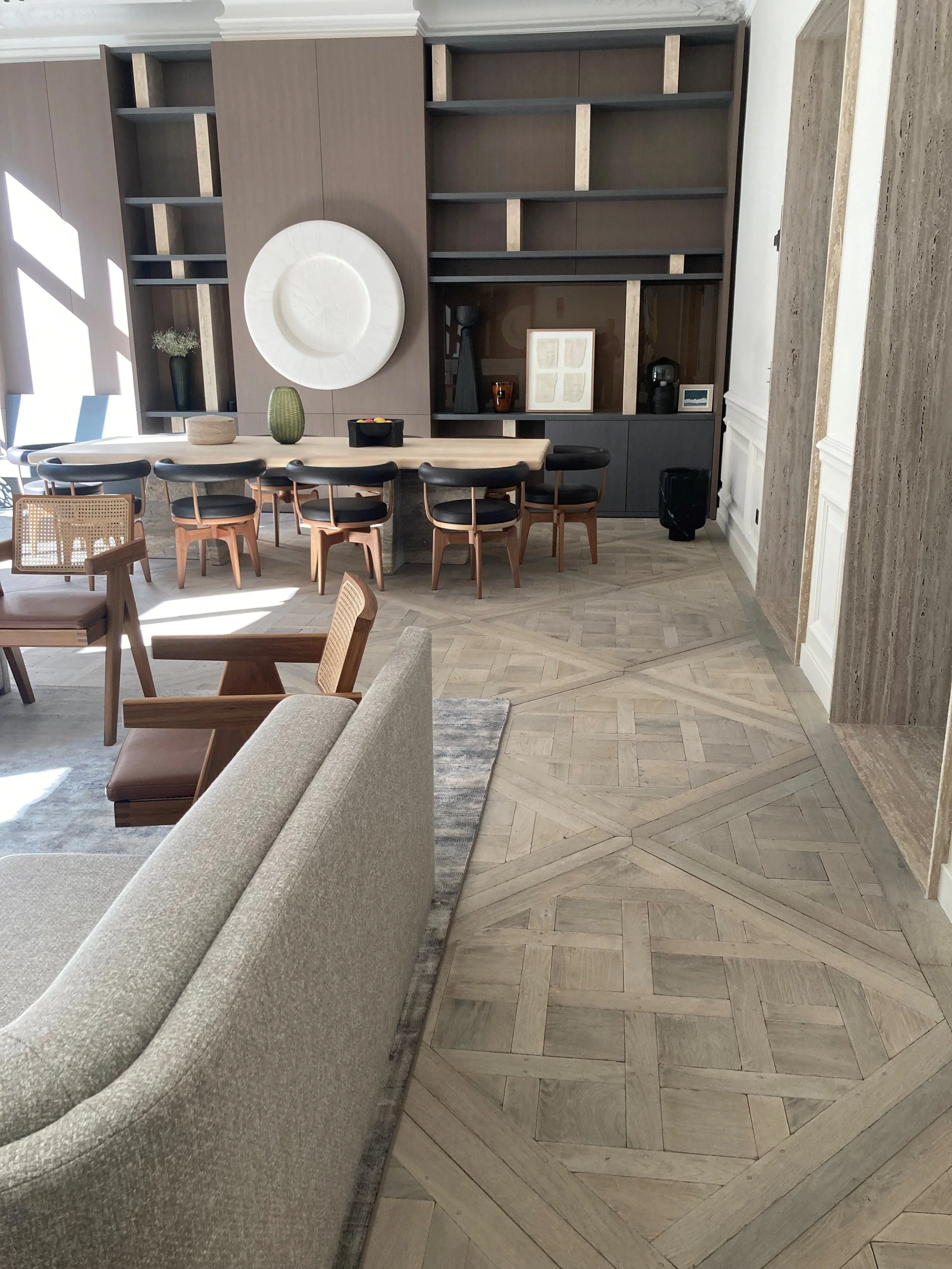 Interior de una sala con mobiliario de madera, una mesa grande y sillas, con libreros en la pared de fondo y decoraciones minimalistas.