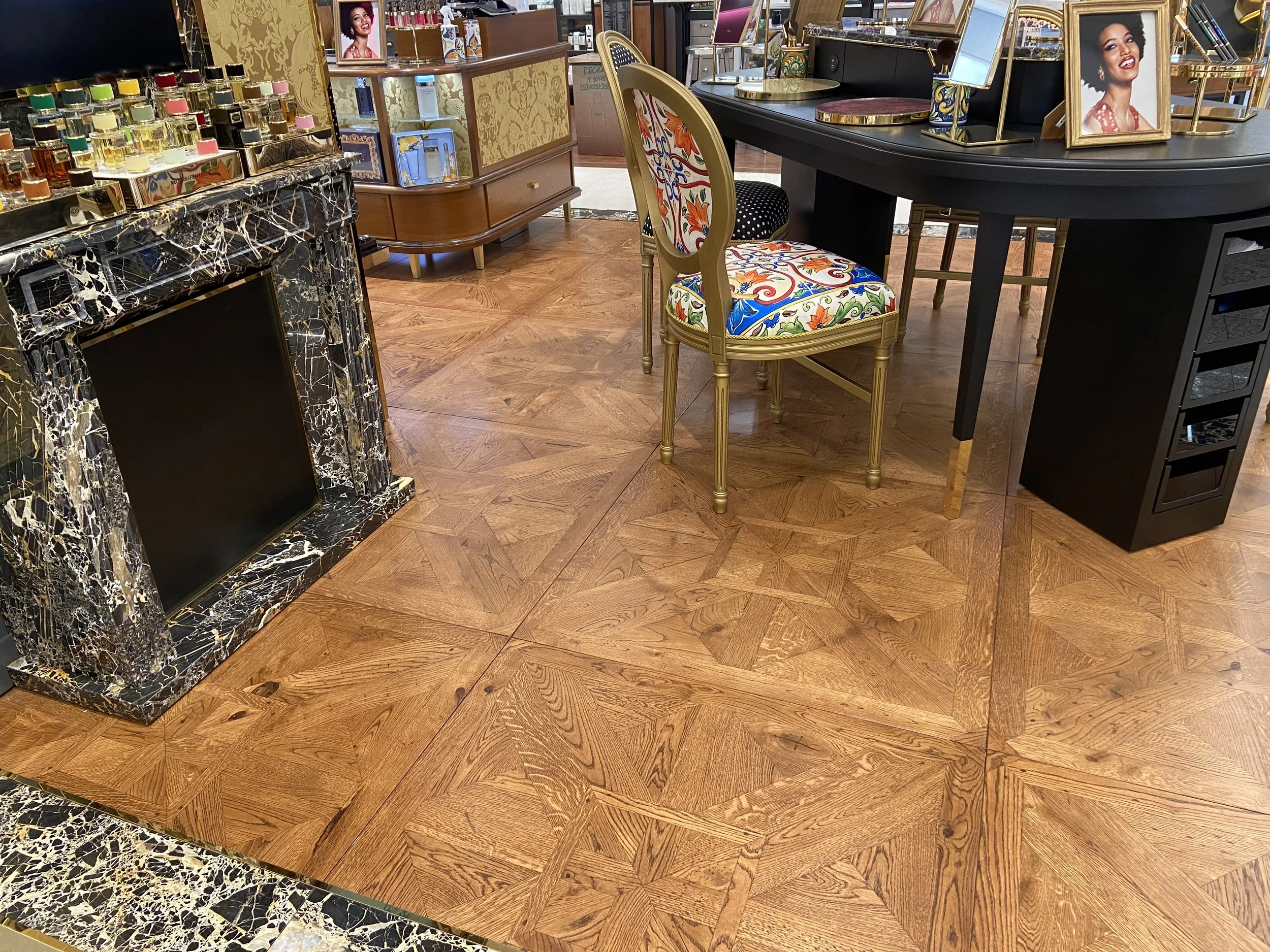 Interior de una tienda o sala decorada con muebles elegantes, un chimenea de mármol negro y madera, un escritorio con fotos enmarcadas, sillas y estantes con productos de perfume y decoración.