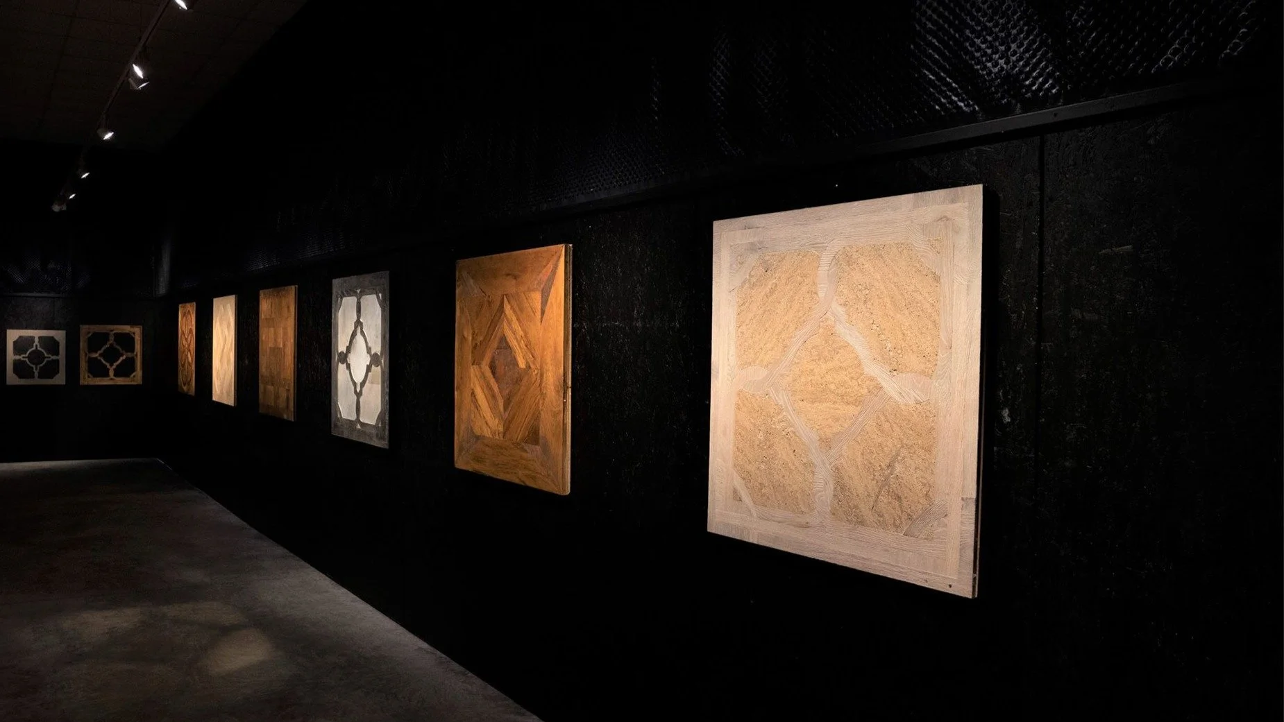 Exposición de cuadros de madera en una galería con muro negro de fondo