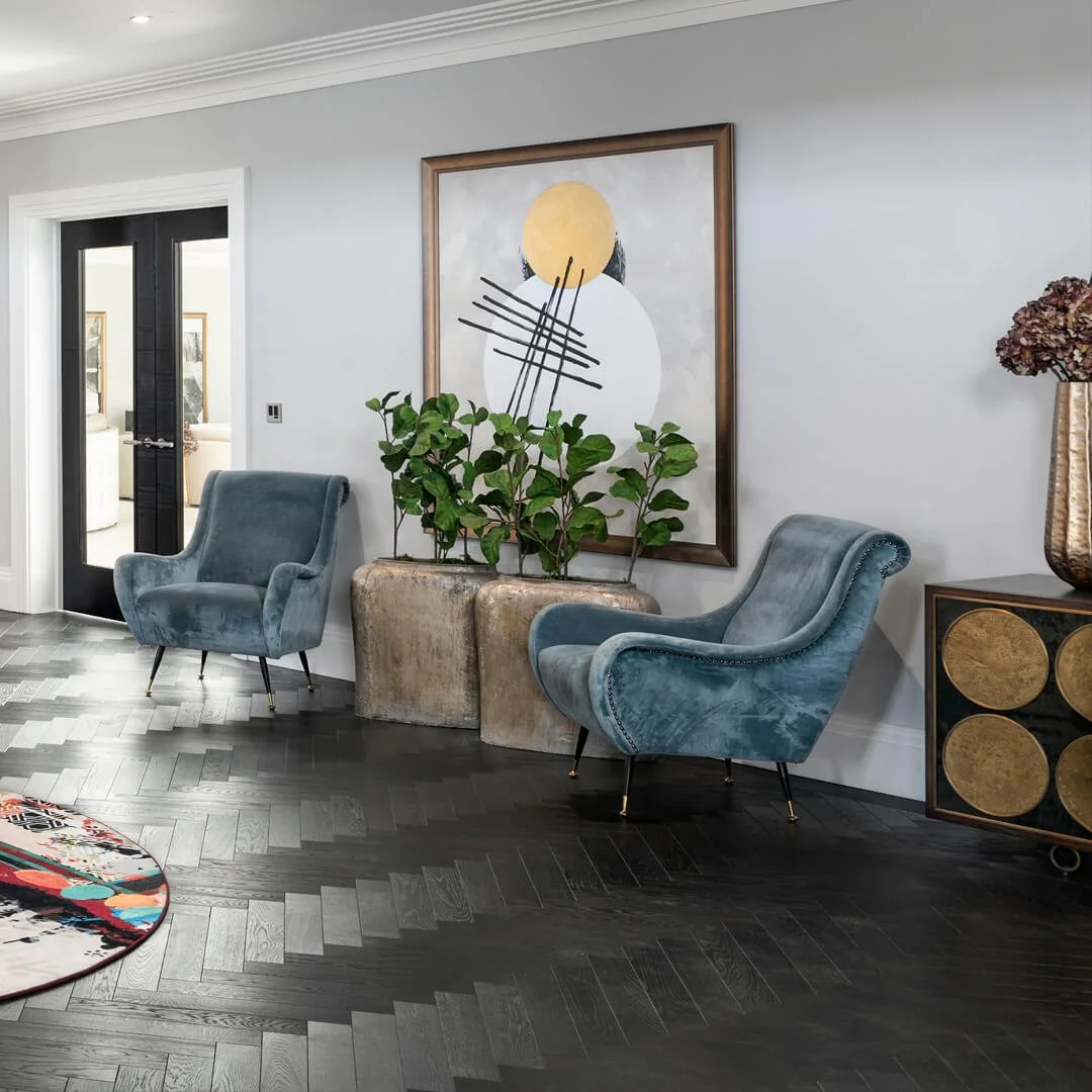 Sala moderna con dos sillones azules, planta en un macetero, cuadro abstracto en la pared, y mueble con decoraciones doradas