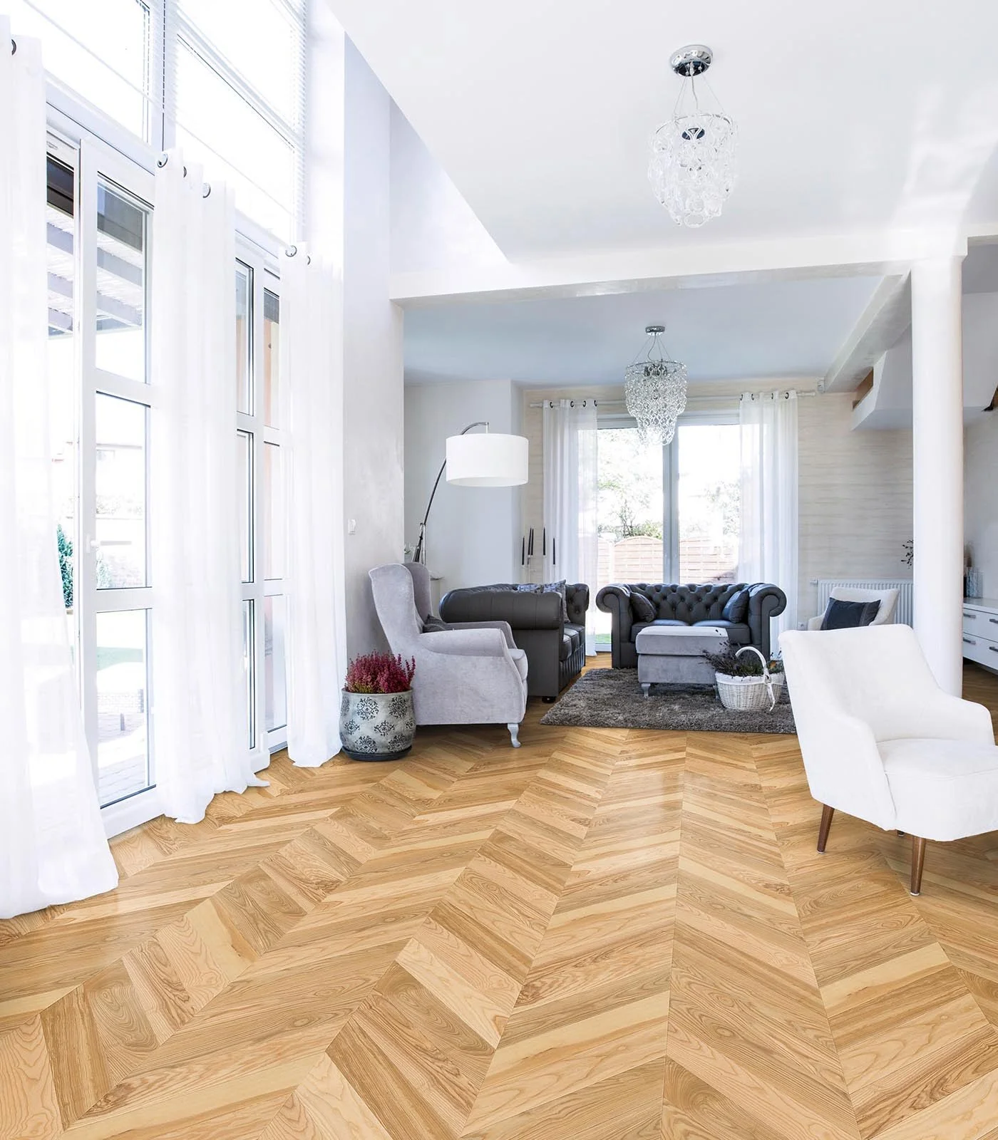 Sala de estar con sillones y cortinas blancas, suelos parquet de madera. tipo chevron punta Hungría, puertas de vidrio con cortinas blancas, lámparas de techo de cristal, y un ambiente luminoso y moderno.