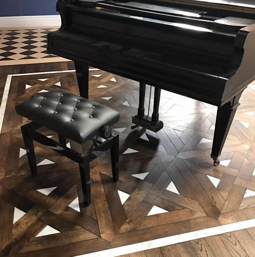 Un piano negro de cola con un banco acolchado negro en un piso de madera decorativo.