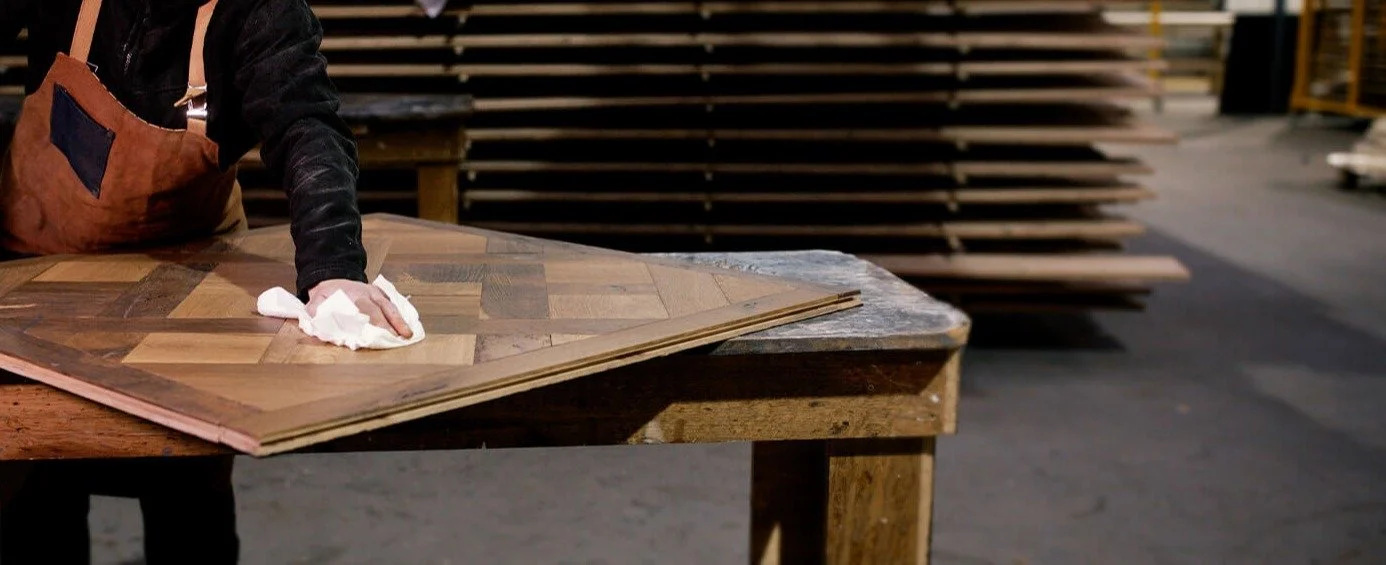 Persona limpiando una mesa de madera con trapo en un taller de carpintería.