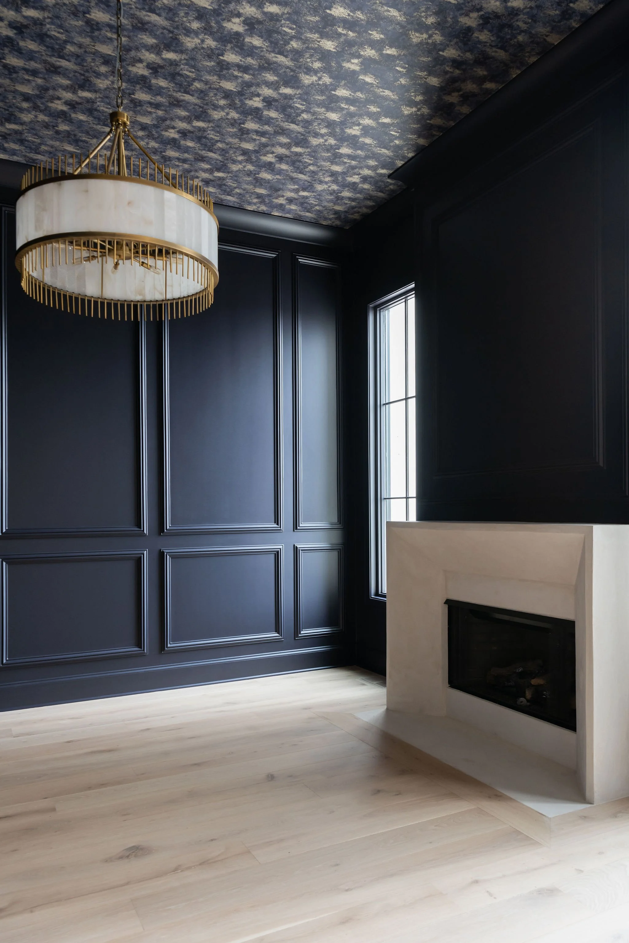 Sala con paredes negras, chimenea y lámpara moderna colgante en el techo, con ventanas que dejan entrar luz natural.