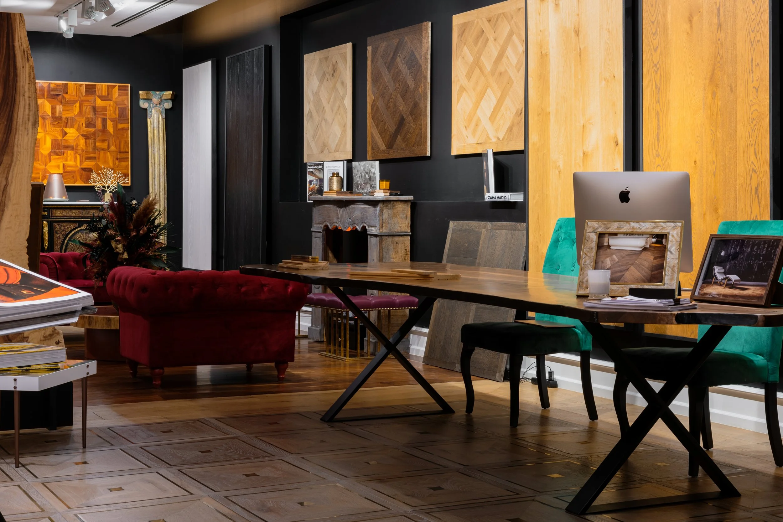 Interior de una sala decorada con paneles de madera en la pared, muebles de color madera oscuro y detalles en dorado, una mesa larga con sillas verdes y negras, un escritorio con una computadora portátil y fotos decorativas, y un sillón de terciopelo