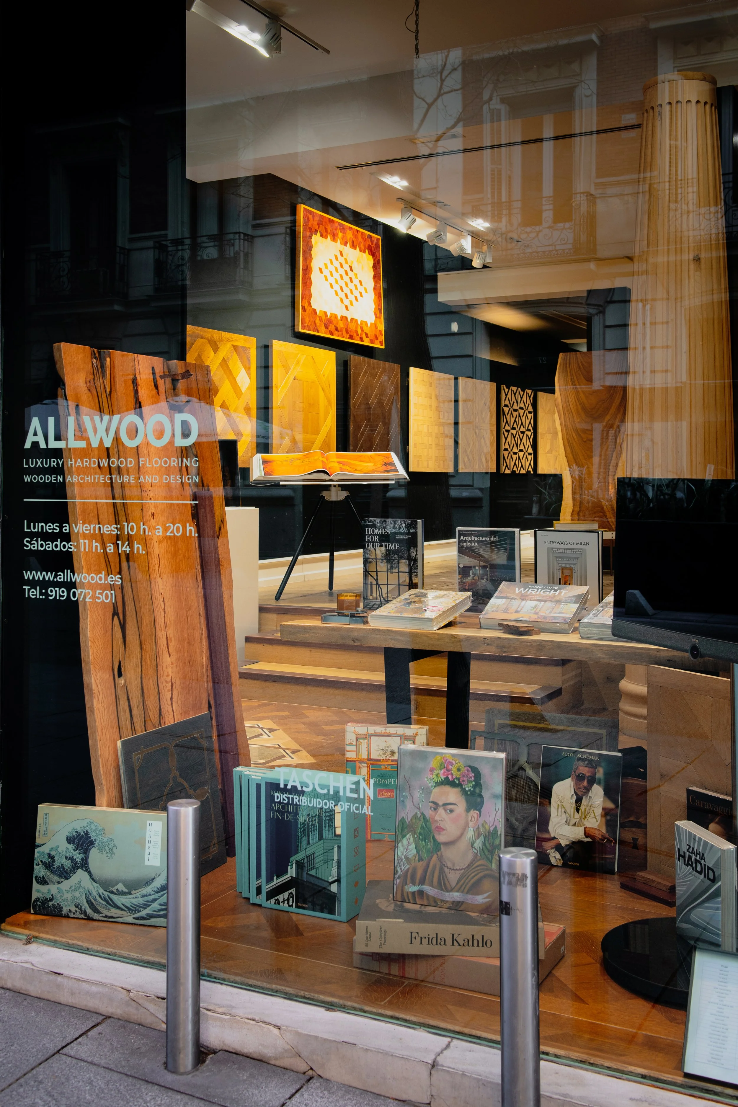Vista de una tienda de suelos parquet de madera. de la marca ALLWOOD con exhibiciones de libros y muestras de madera en el interior, visible a través del cristal de la ventana.