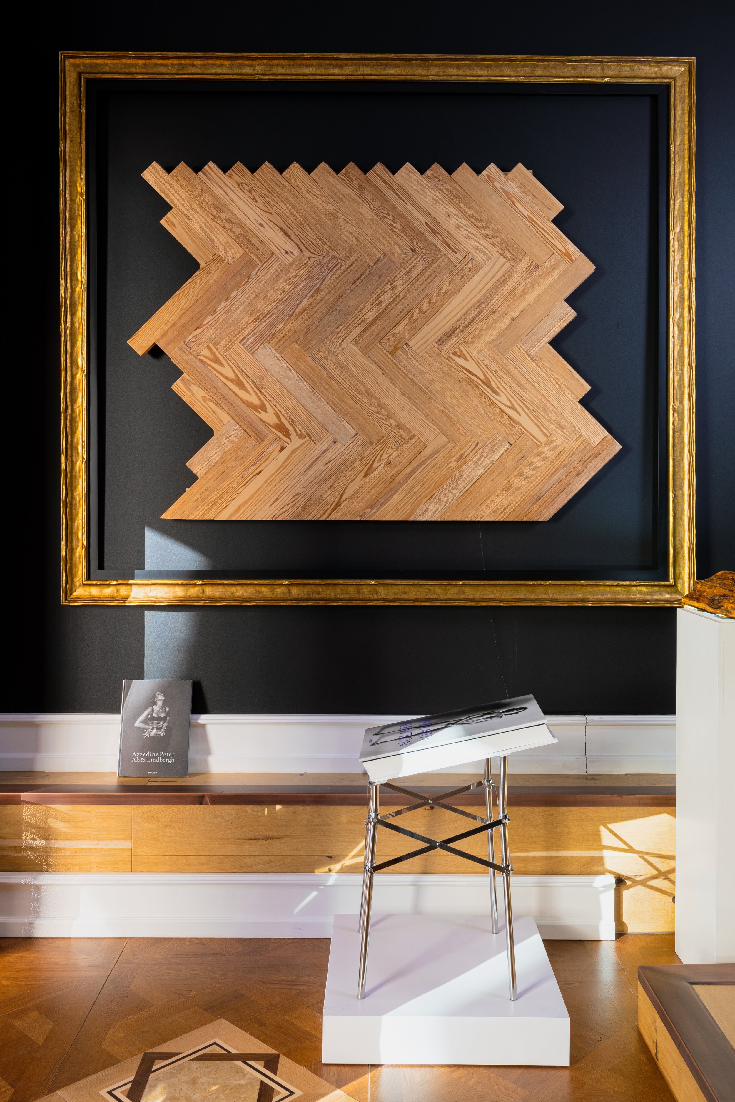 Cuadro de madera pino melis americano recuperado en formato espiga recta sobre fondo negro, exhibido en una galería con suelo de madera y una pértiga moderna de exhibición.