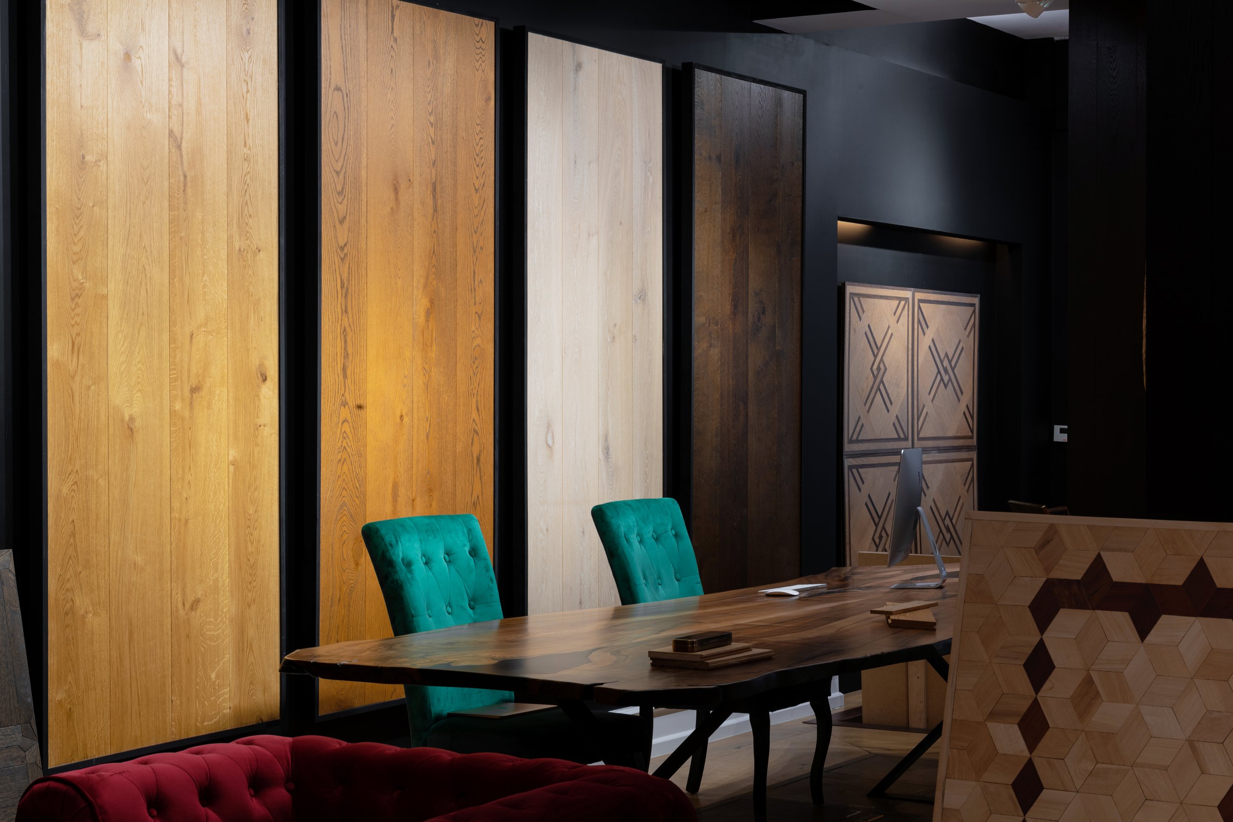 Sala de reuniones con un escritorio de madera, sillas verdes, paredes con paneles de madera en diferentes tonos, y decoración moderna.
