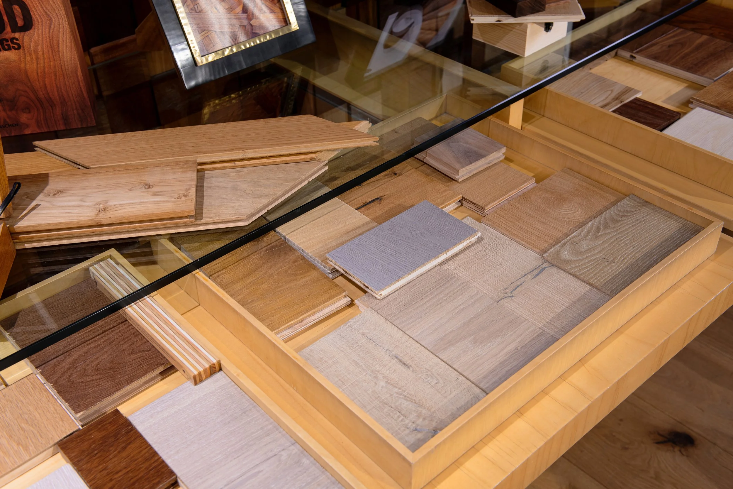 Muestras de diferentes tipos de madera en una mesa de exhibición con tapa de cristal.