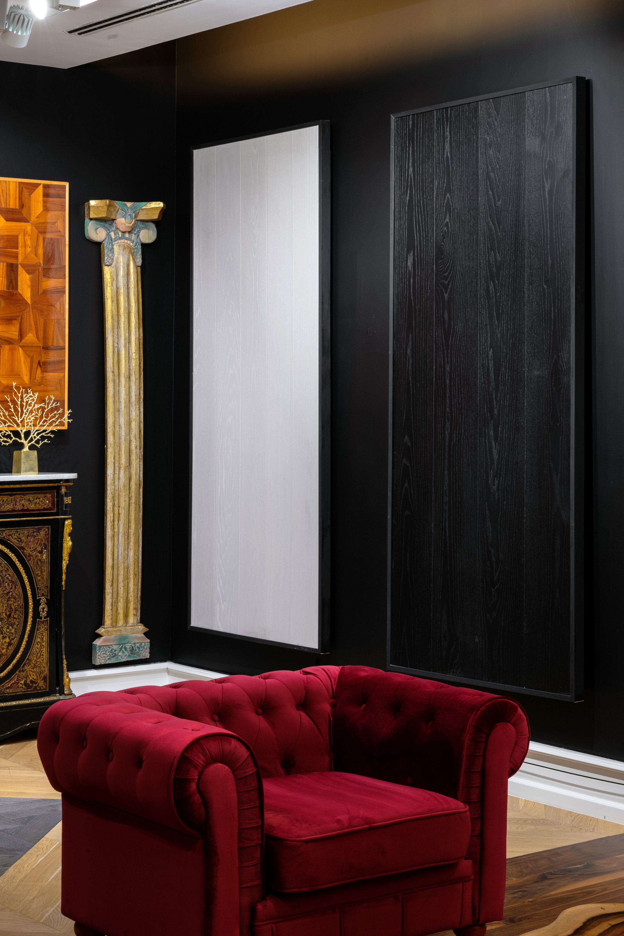 Sofá de terciopelo rojo en una sala de estilo clásico con paredes negras y cuadros decorativos negros y blancos en la pared.