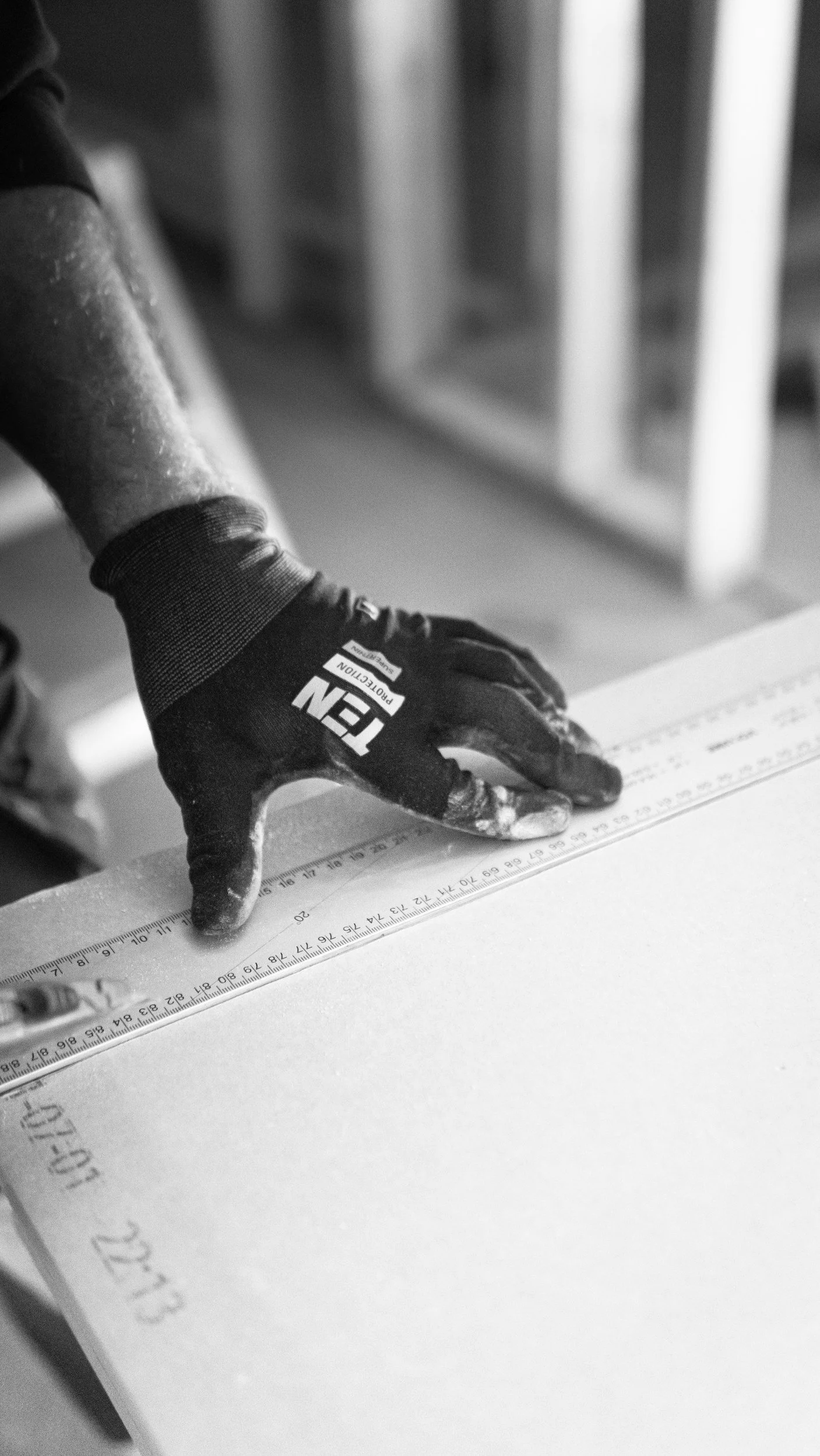 Una mano con guante ajustando una regla en una mesa de trabajo.