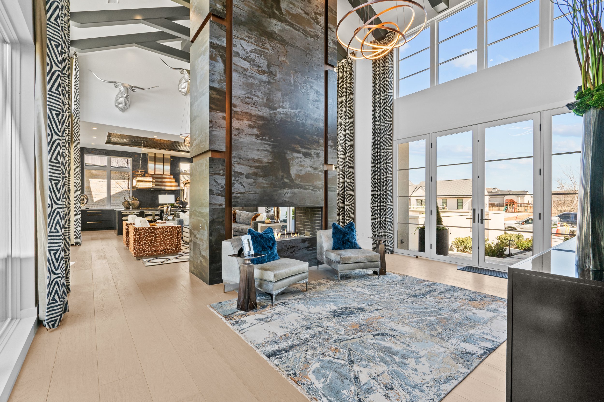 Sala de estar moderna con paredes de grandes ventanas, cortinas con patrón geométrico y muebles elegantes, decorada con alfombra y cojines azules.