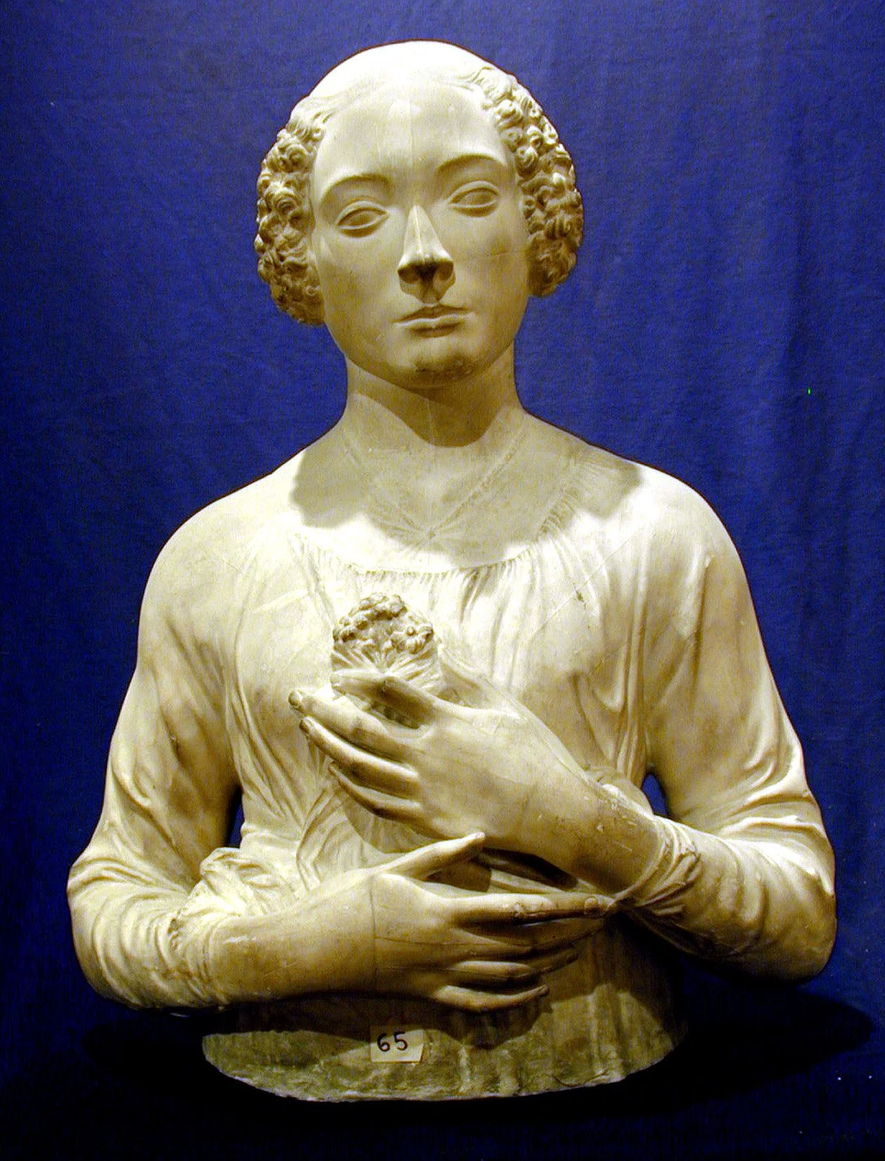 Escultura de una mujer con cabello rizado y expresión serena, sosteniendo un corazón en su pecho, con fondo azul.