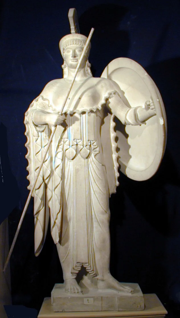 Estatua de una figura humana vestida con ropa tradicional y armada con una lanza y un escudo.