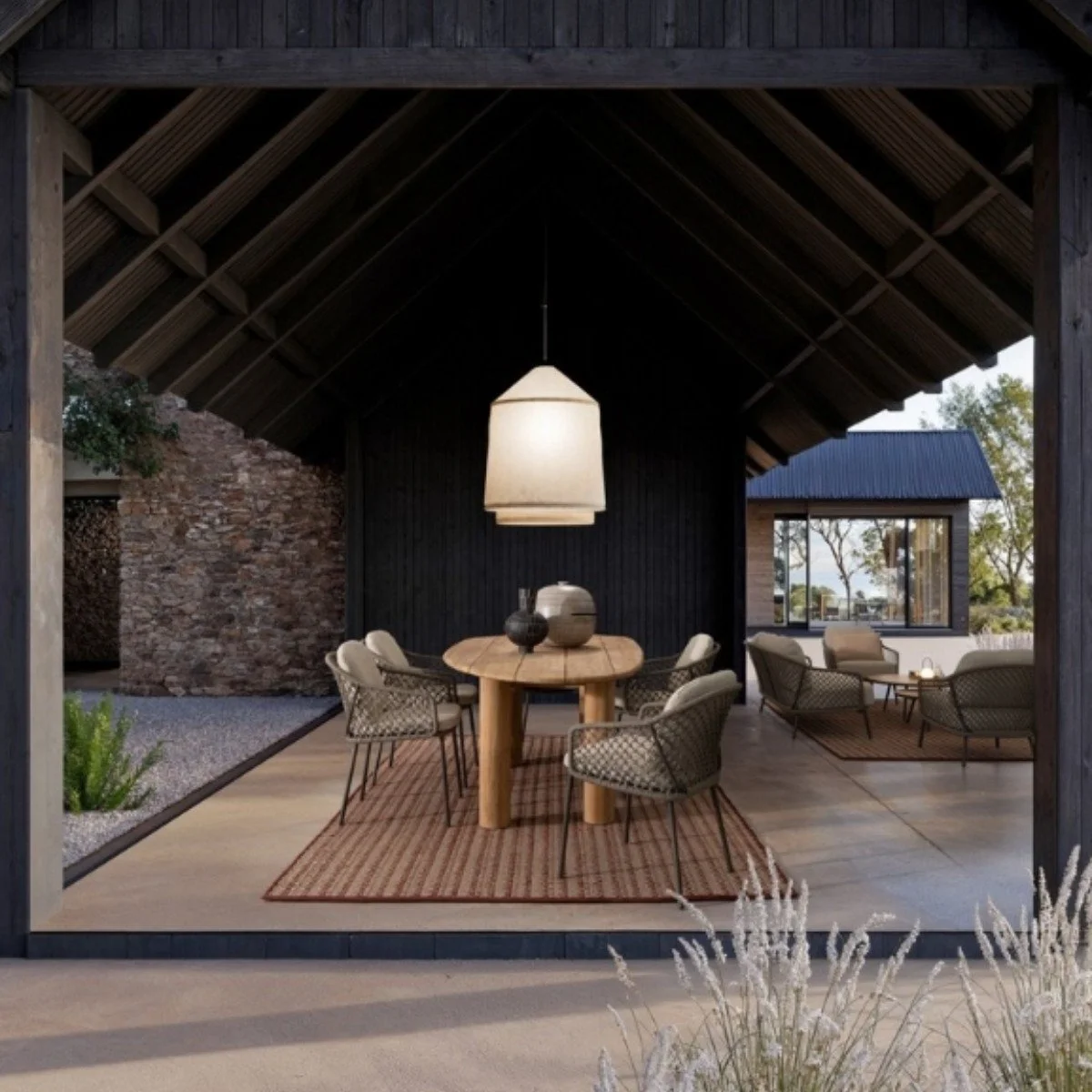 Espacio de descanso al aire libre con comedor y sala, techo de madera, lámpara grande, muebles de mimbre y decoración moderna.