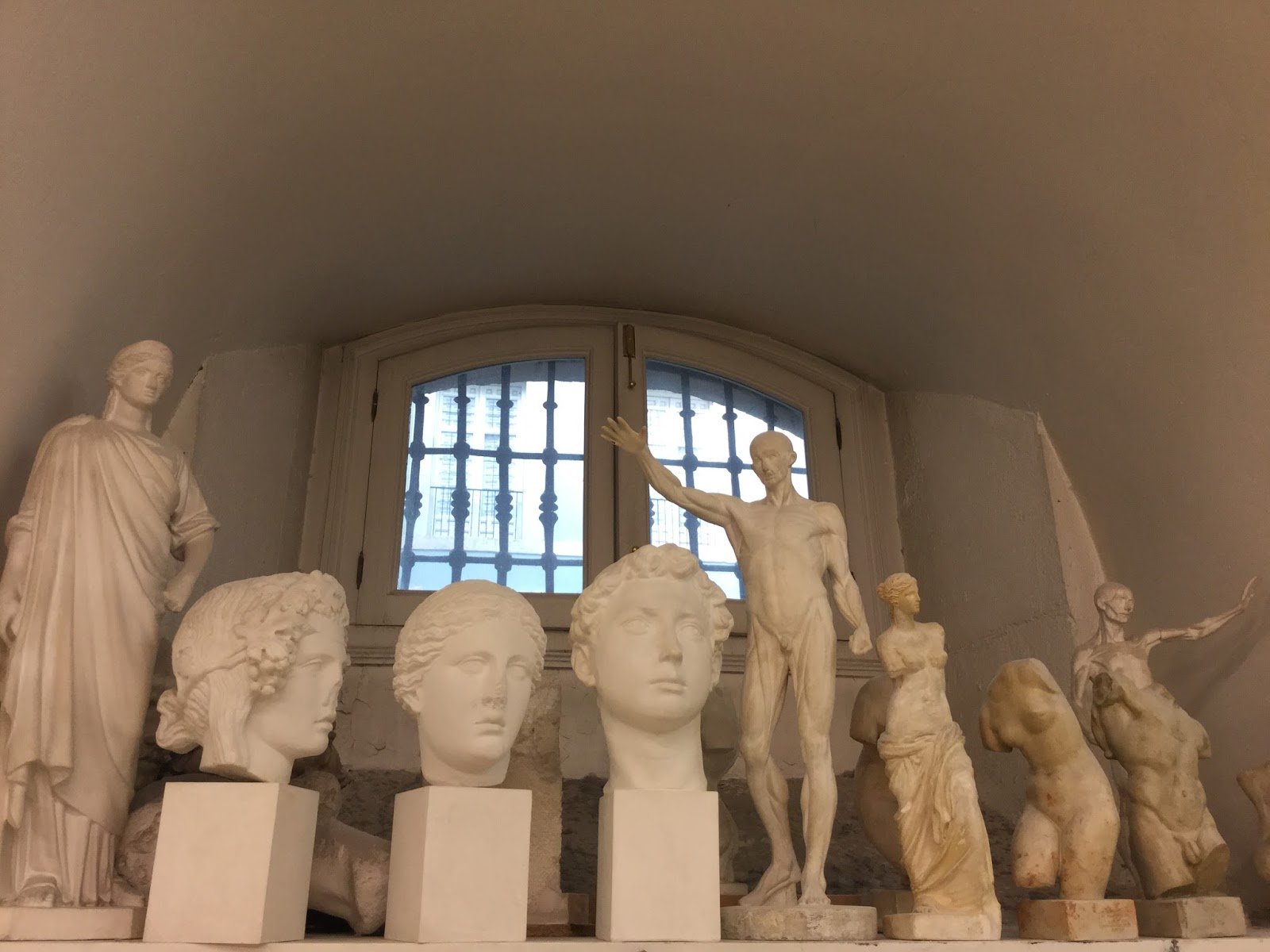 Esculturas clásicas en una habitación con ventana con rejas.