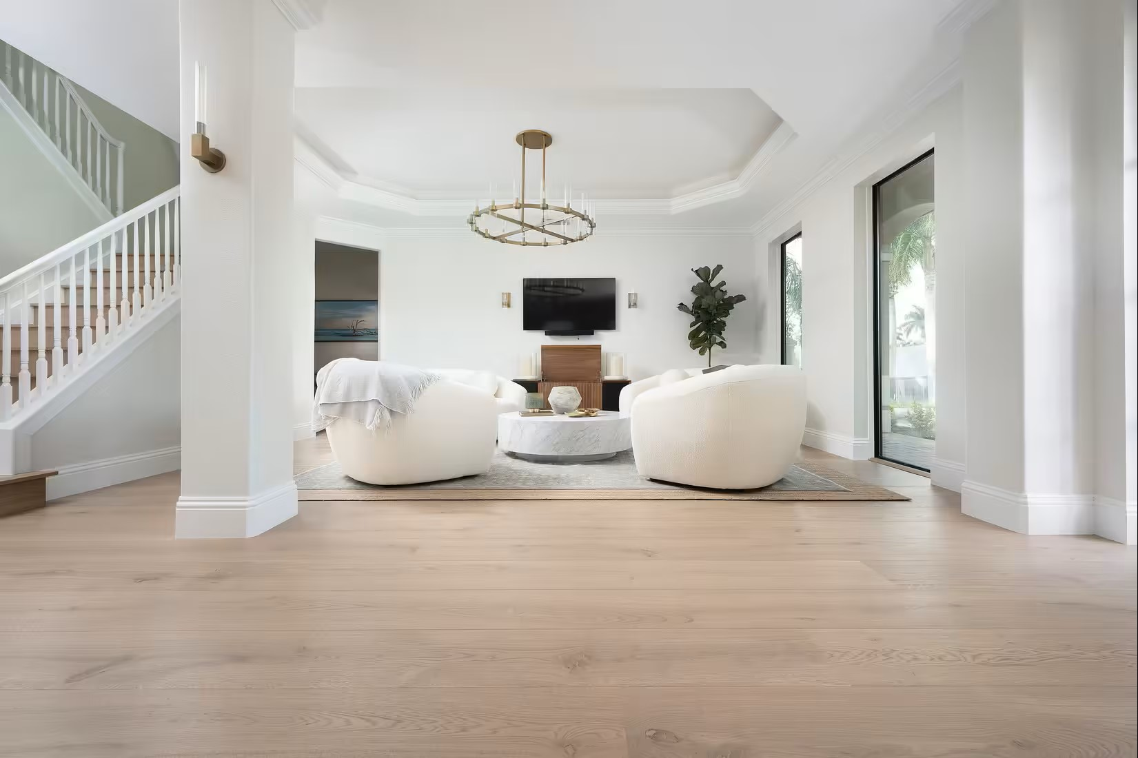 suelos de madera en sala de estar con sillones blancos, mesa central de mármol, un televisor en la pared y plantas decorativas, con paredes blancas y ventanales grandes.