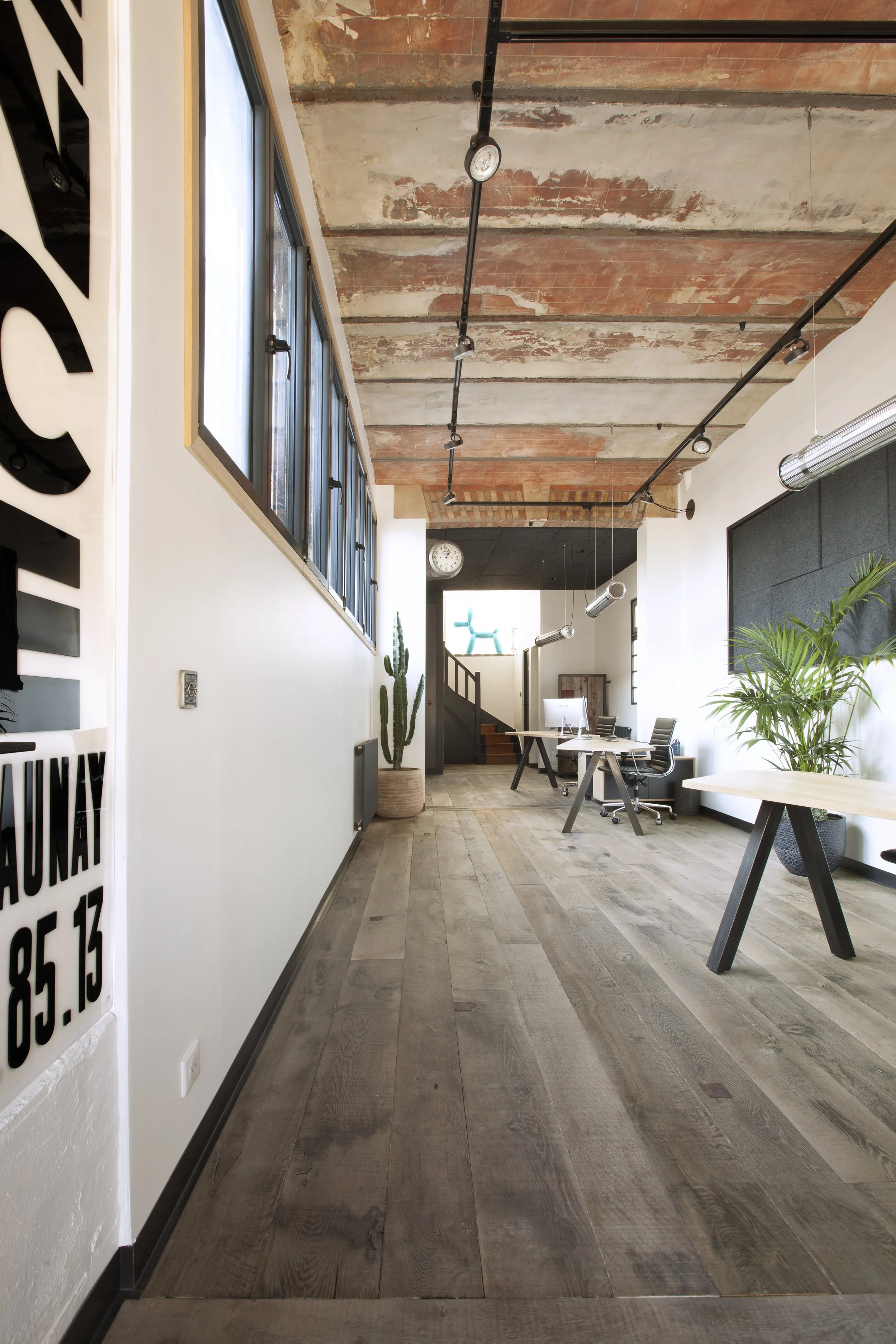 Oficina moderna con madera en el suelo, plantas verdes, sillas de oficina y ventanas grandes.