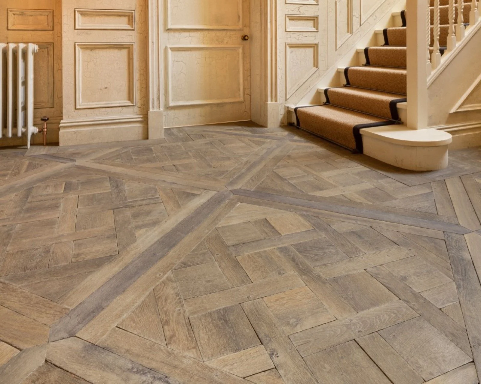 Suelo de madera en un pasillo con escaleras y paredes de madera pintada en tonos beige.