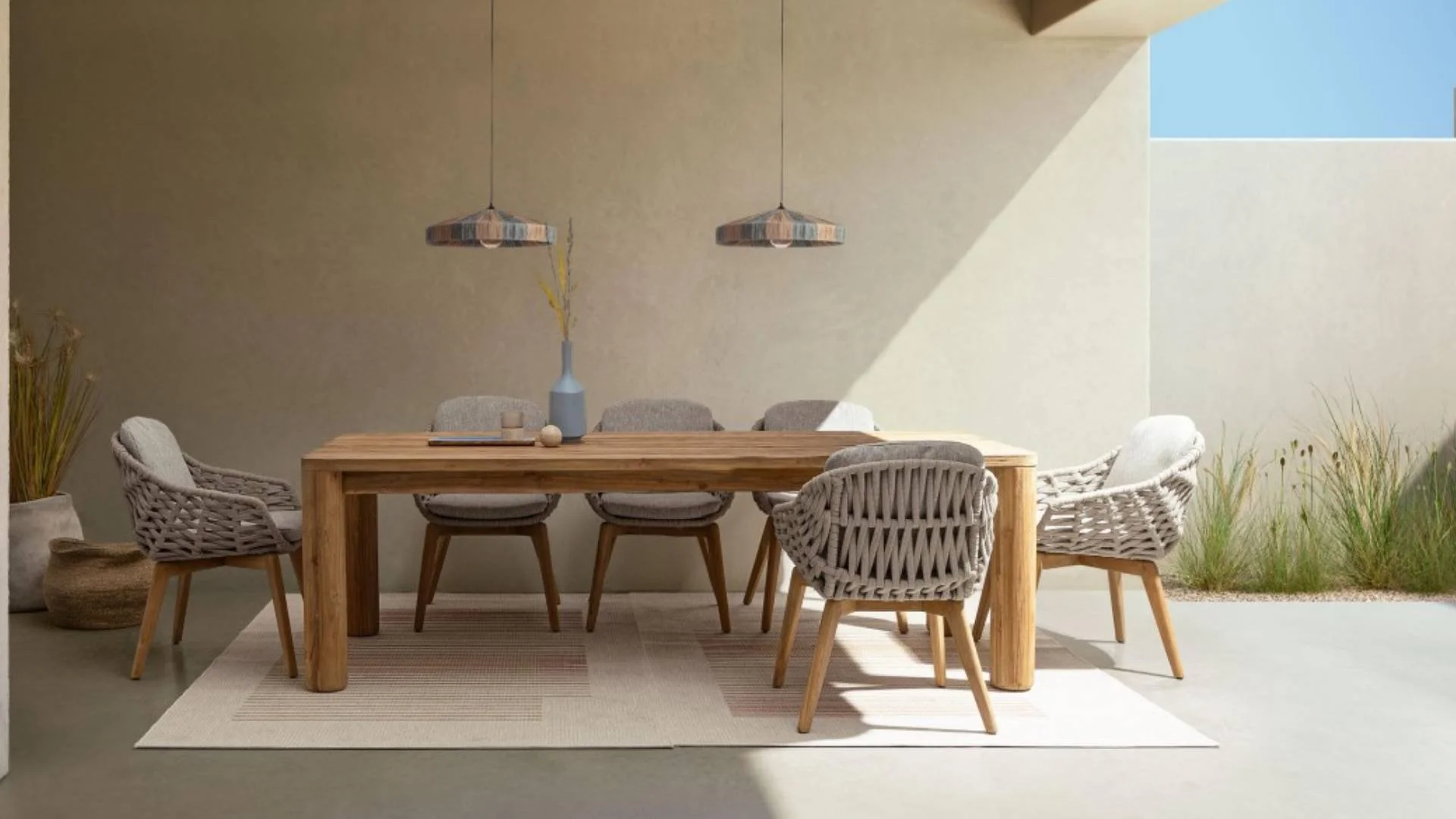 Comedor con mesa de madera y sillas tapizadas en tonos neutros, colgantes decorativos y plantas ornamentales en un espacio con luz natural.