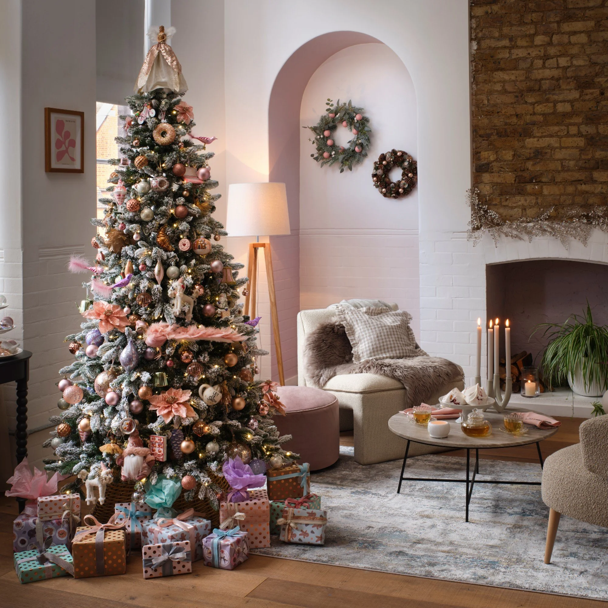 Árbol de Navidad decorado con adornos rosados, dorados y plateados, rodeado de regalos envueltos y decoraciones en un salón elegante con chimenea y decoraciones navideñas.