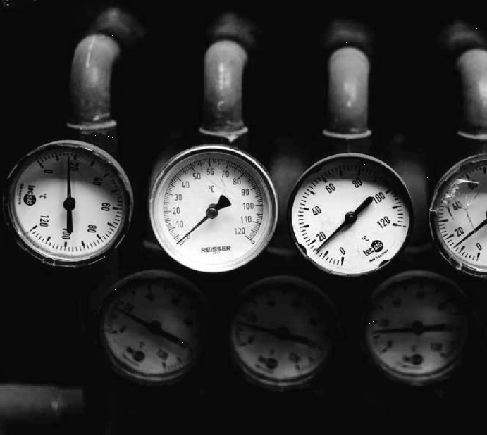 Cuatro manómetros y cuatro tuberías de metal en una consola de control industrial.