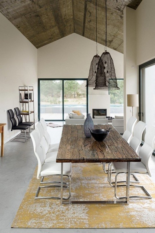 Interiores de sala moderna con comedor, techo de concreto, mesas de madera, sillas blancas y decoraciones minimalistas.