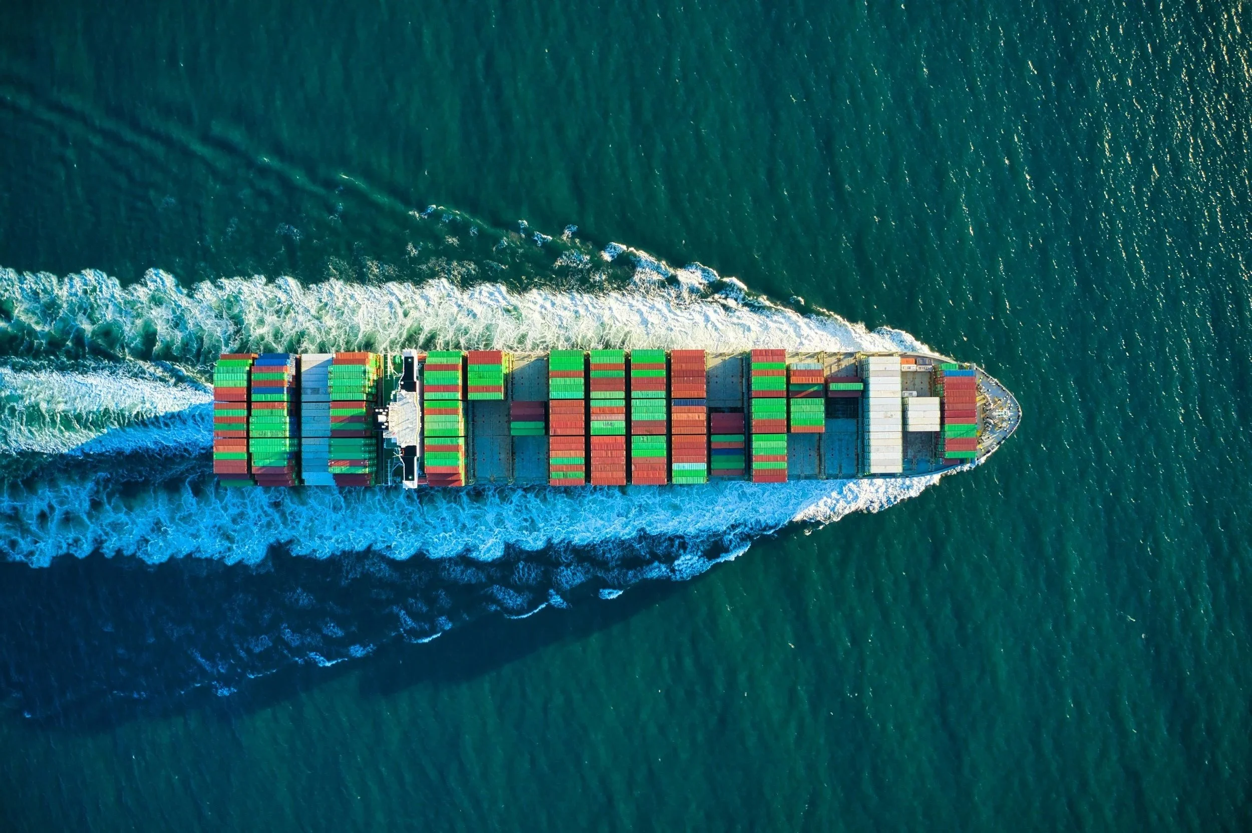 Aerial view of a large cargo ship with numerous colorful containers moving through the ocean.