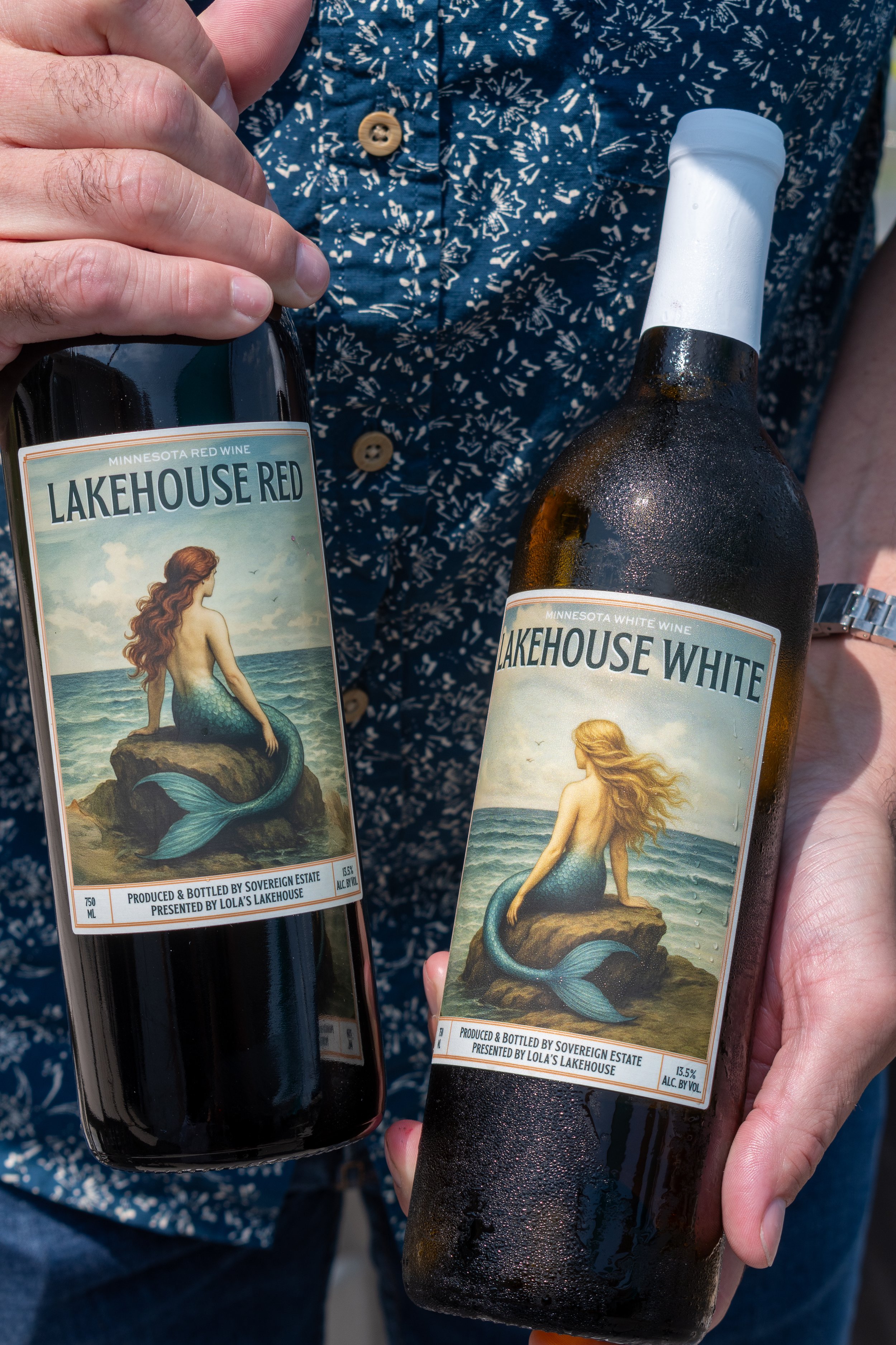 Close-up of a person holding two bottles of Lola's Lakehouse house wine with labels featuring a mermaid illustration designed by Social Construct Media & Design.