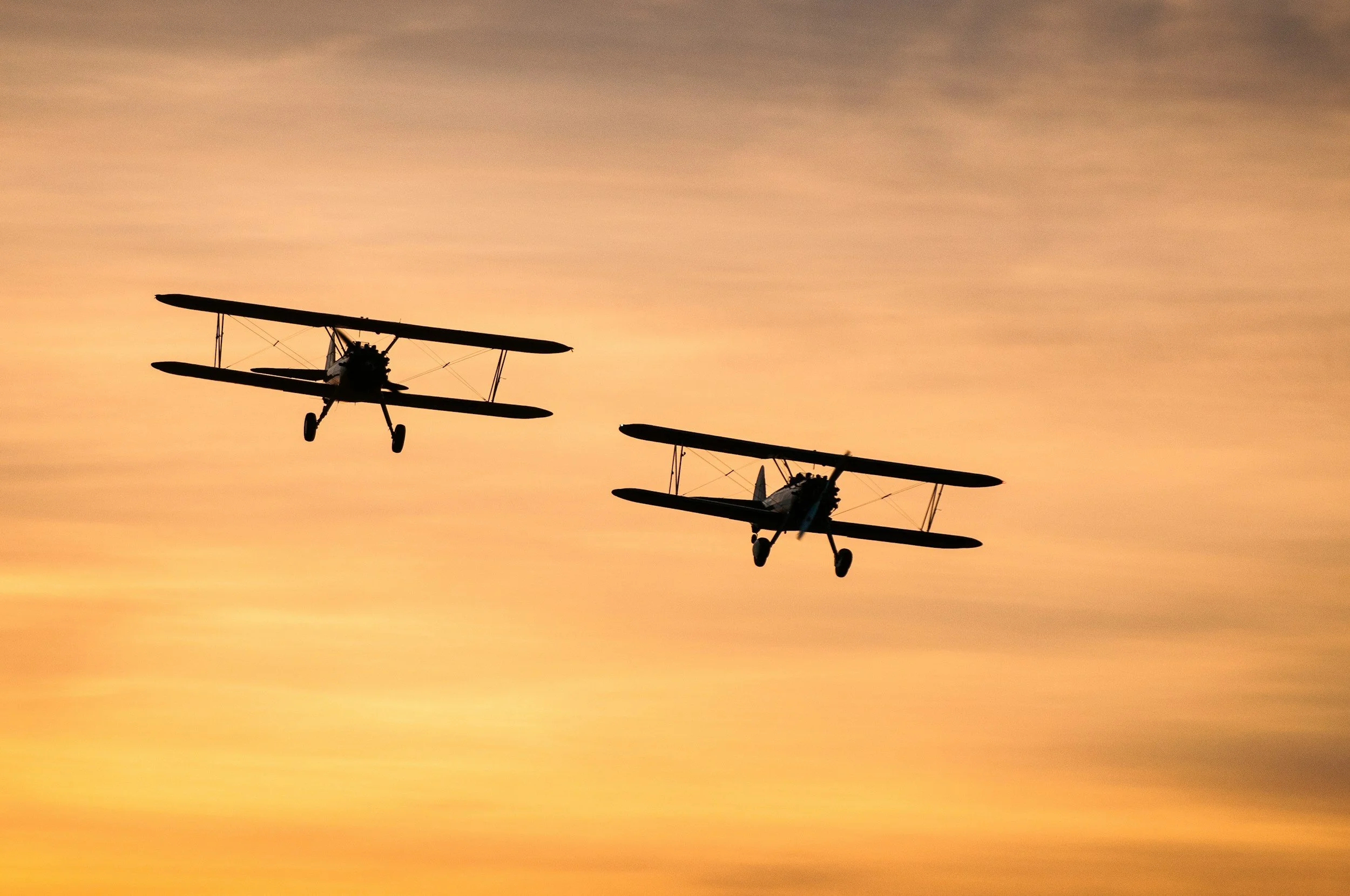 Two vintage biplanes flying against a colorful sunset sky.