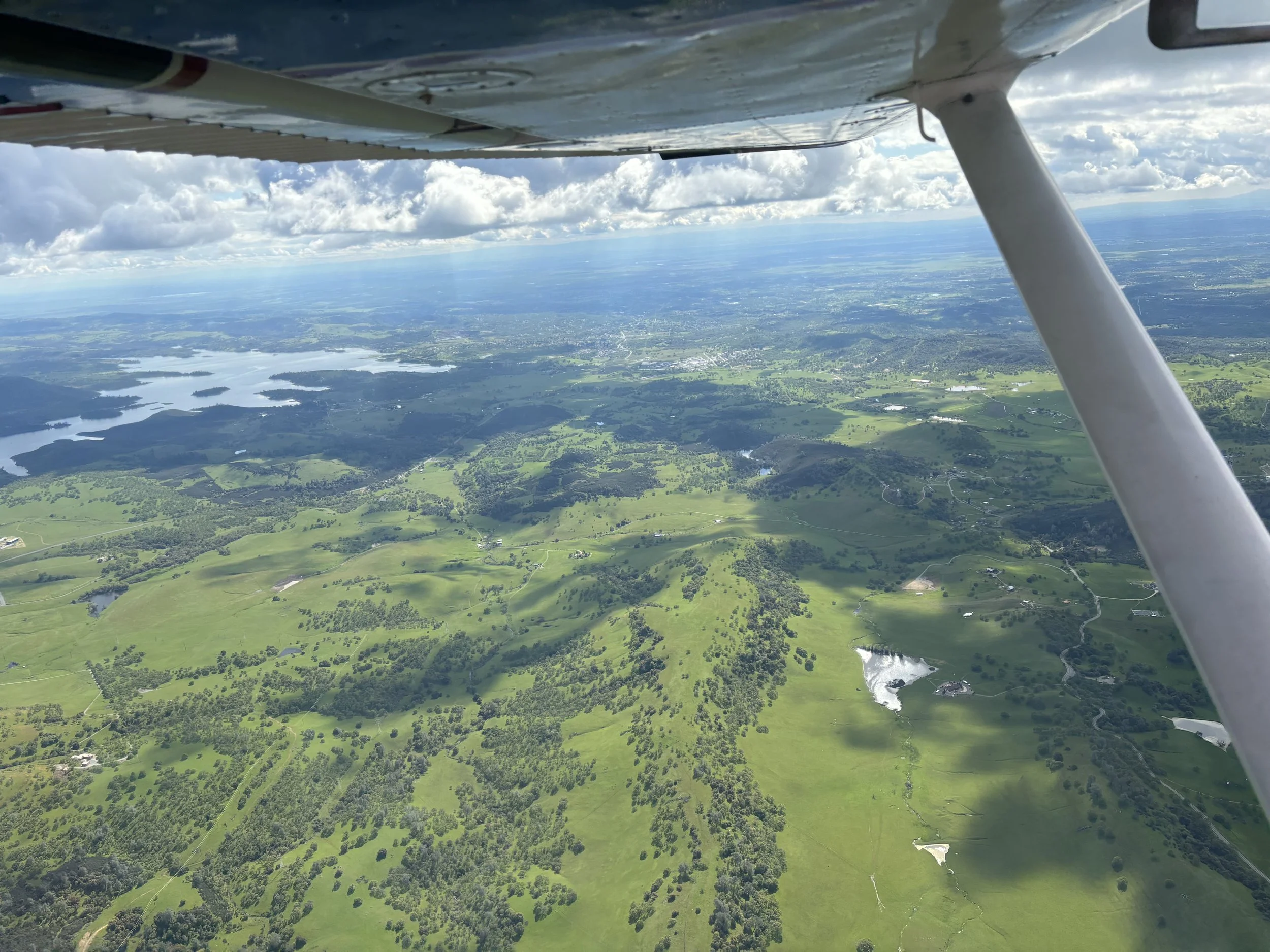 Aerial view of green farmland with lakes and scattered trees seen from a small airplane flying high in the sky.