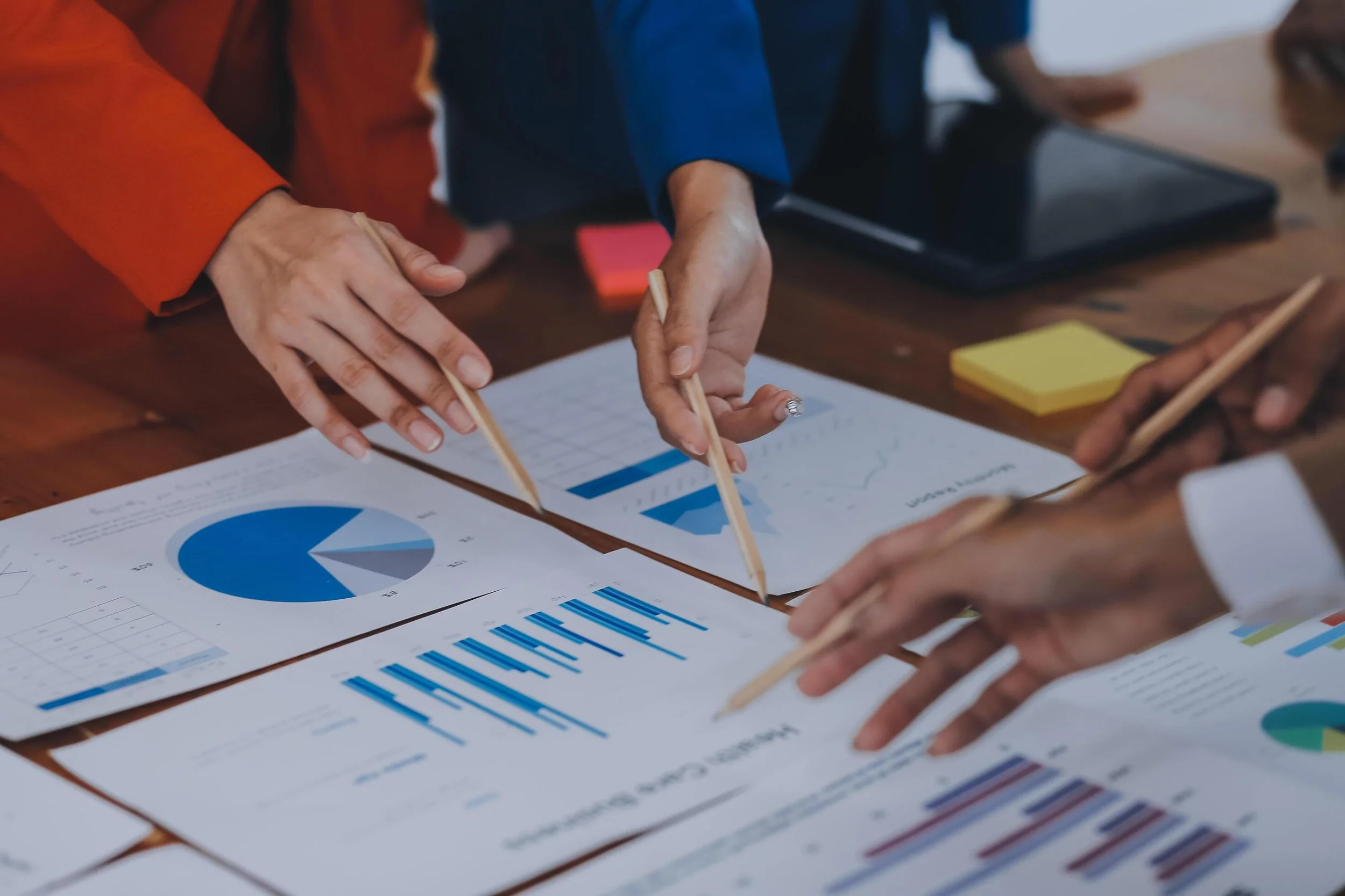 Mensen bespreken grafieken en rapporten met pie- en staafdiagrammen op een vergadertafel.