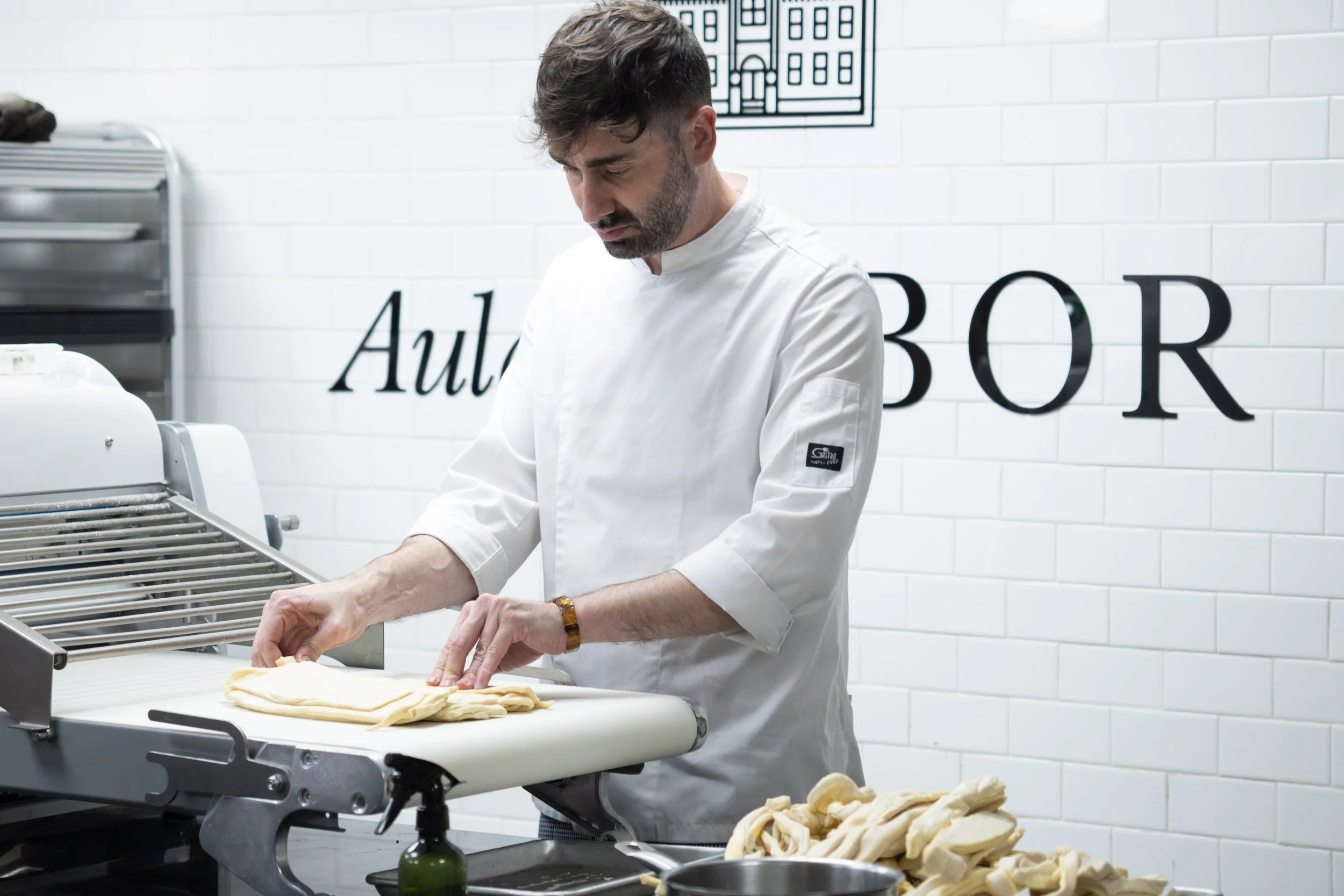Chef pastelero trabajando la masa de croissant en una laminadora, para laminar y dar pliegues