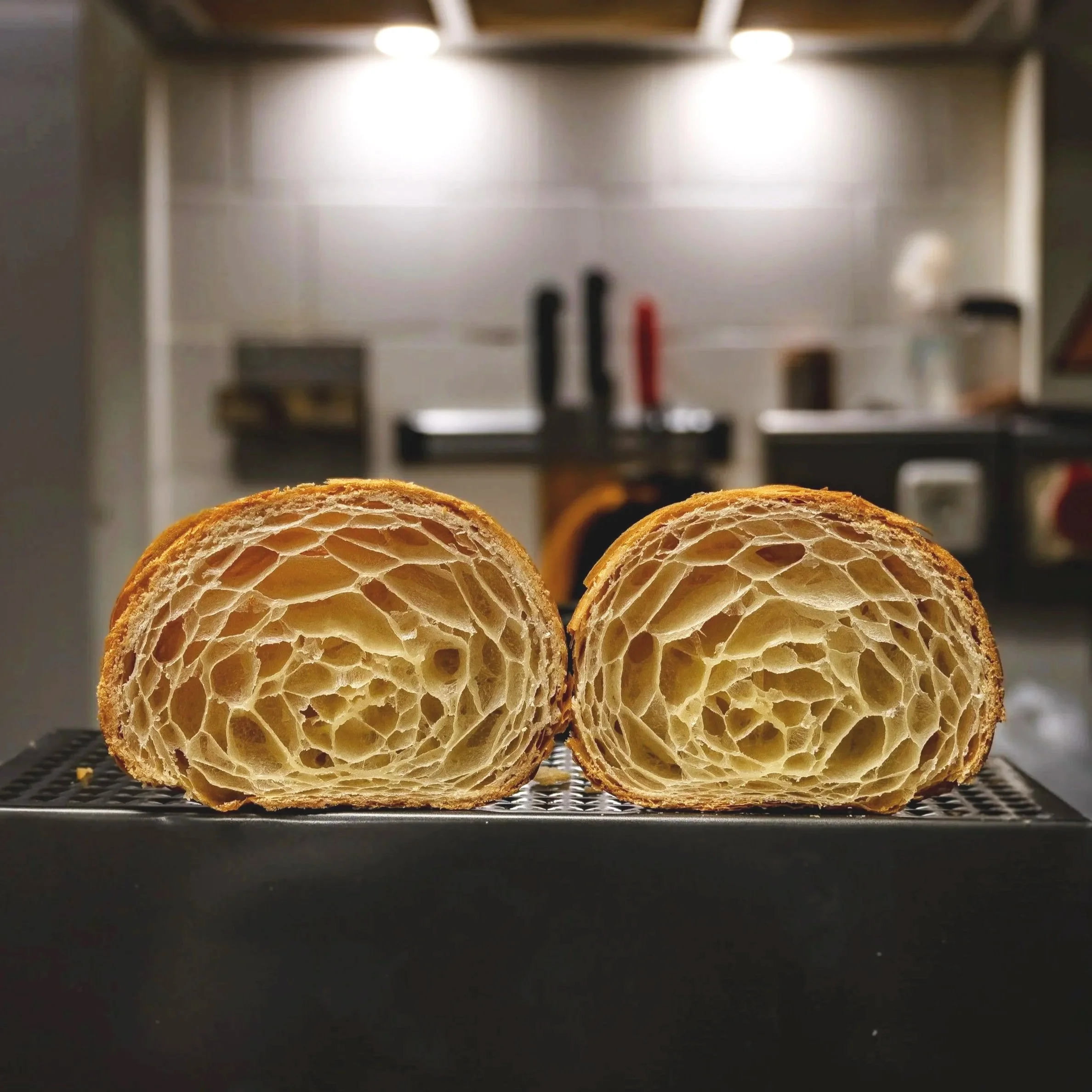 Pan de croissant cortado por la mitad mostrando su textura aireada en un ambiente de cocina.