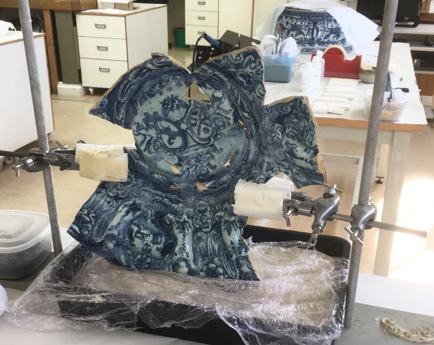 Ceramic maiolica plate in a conservation workshop / lab. Museum-quality ceramics conservation services in San Francisco, CA. Edge-bonding a broken earthenware platter in a conservation studio. Repair and restoration of antique ceramic pottery. SF.