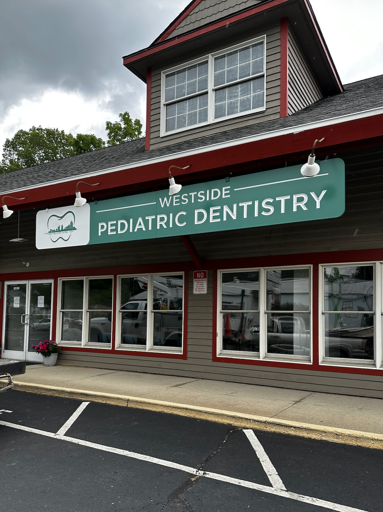 Exterior of a building with a sign that reads 'Westside Pediatric Dentistry,' showing windows, a parking lot, and a cloudy sky.