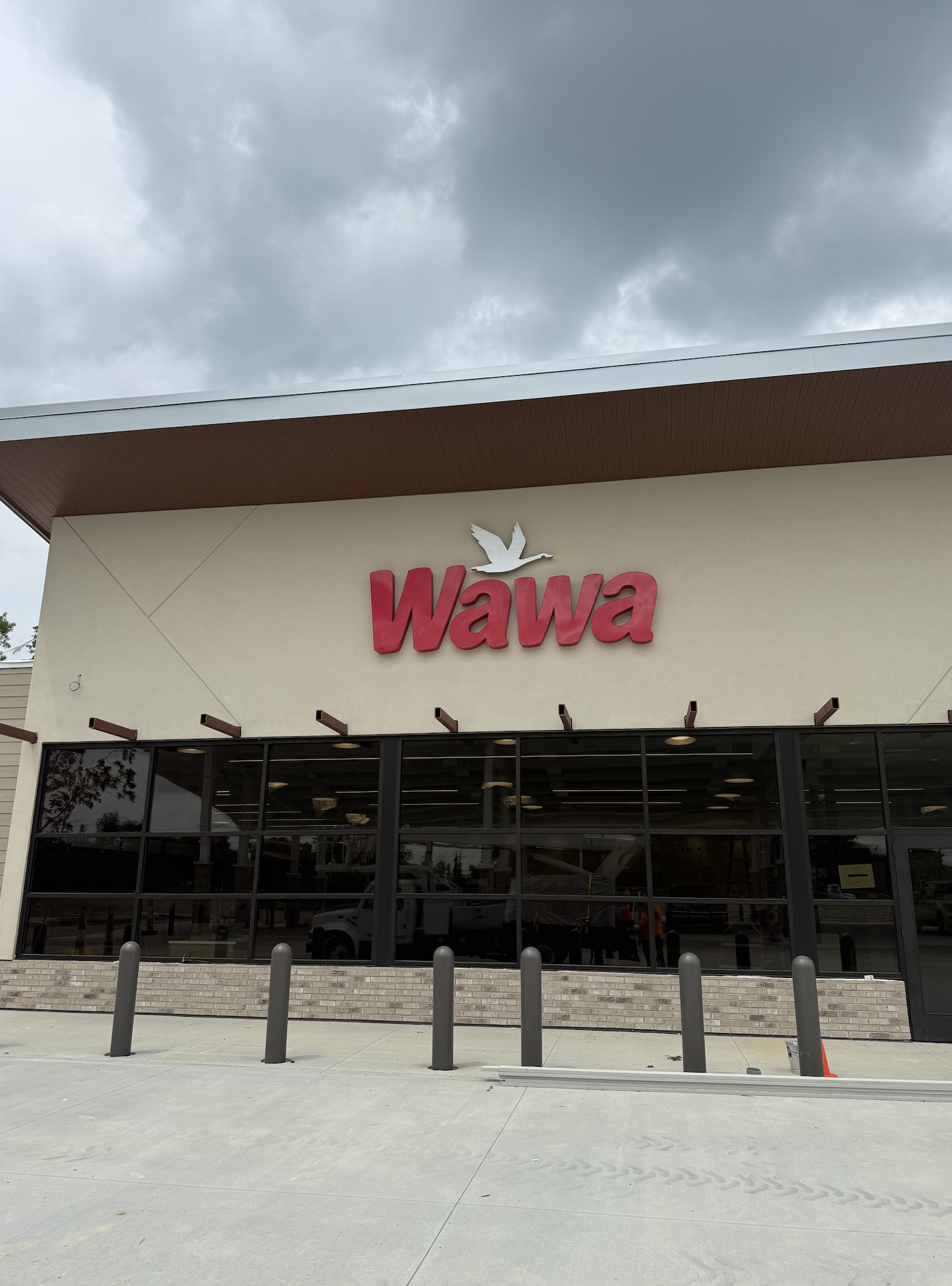 Exterior of a Wawa convenience store with large red sign and a white flying bird logo above the entrance, set against a cloudy sky.