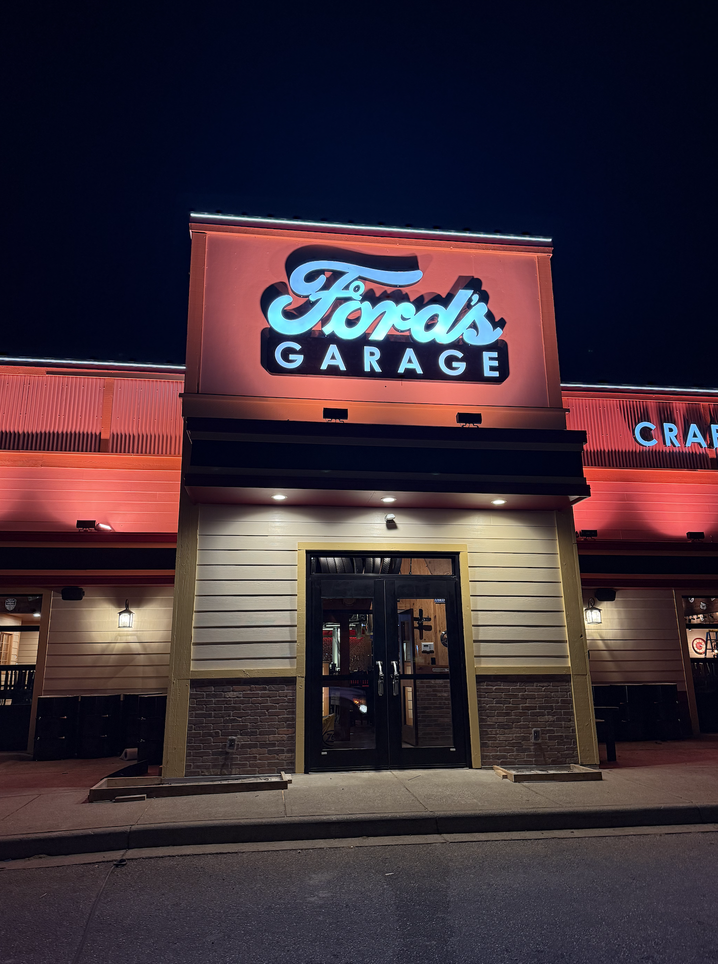 Nighttime view of the exterior of Ford's Garage restaurant with illuminated sign, entrance doors, and sidewalk.