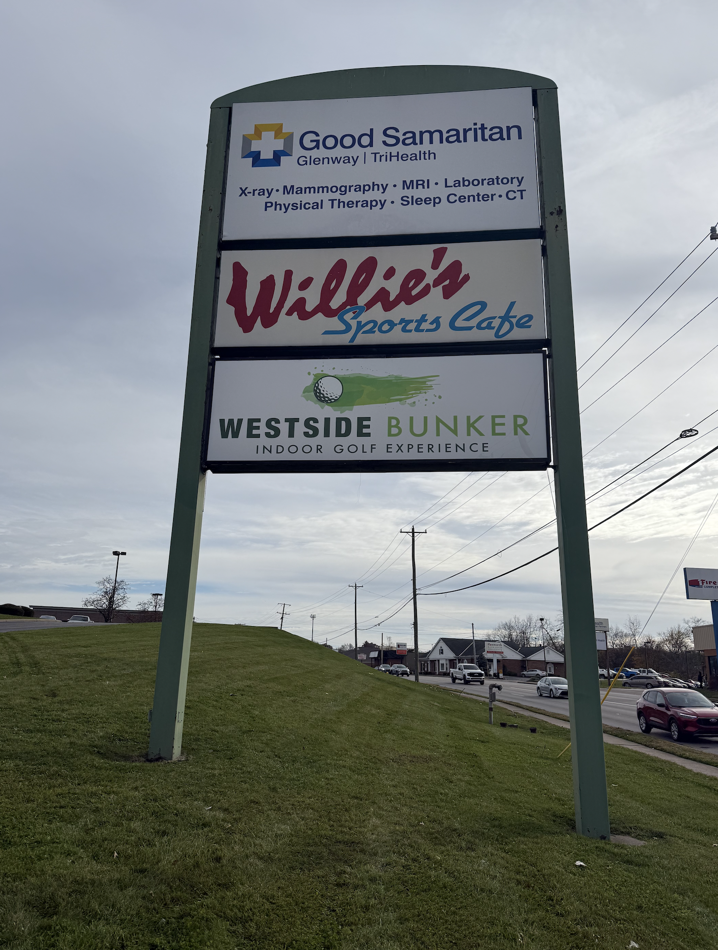 A roadside sign with four business advertisements: Good Samaritan medical services, Willie's Sports Cafe, Westside Bunker indoor golf, and a fire department.